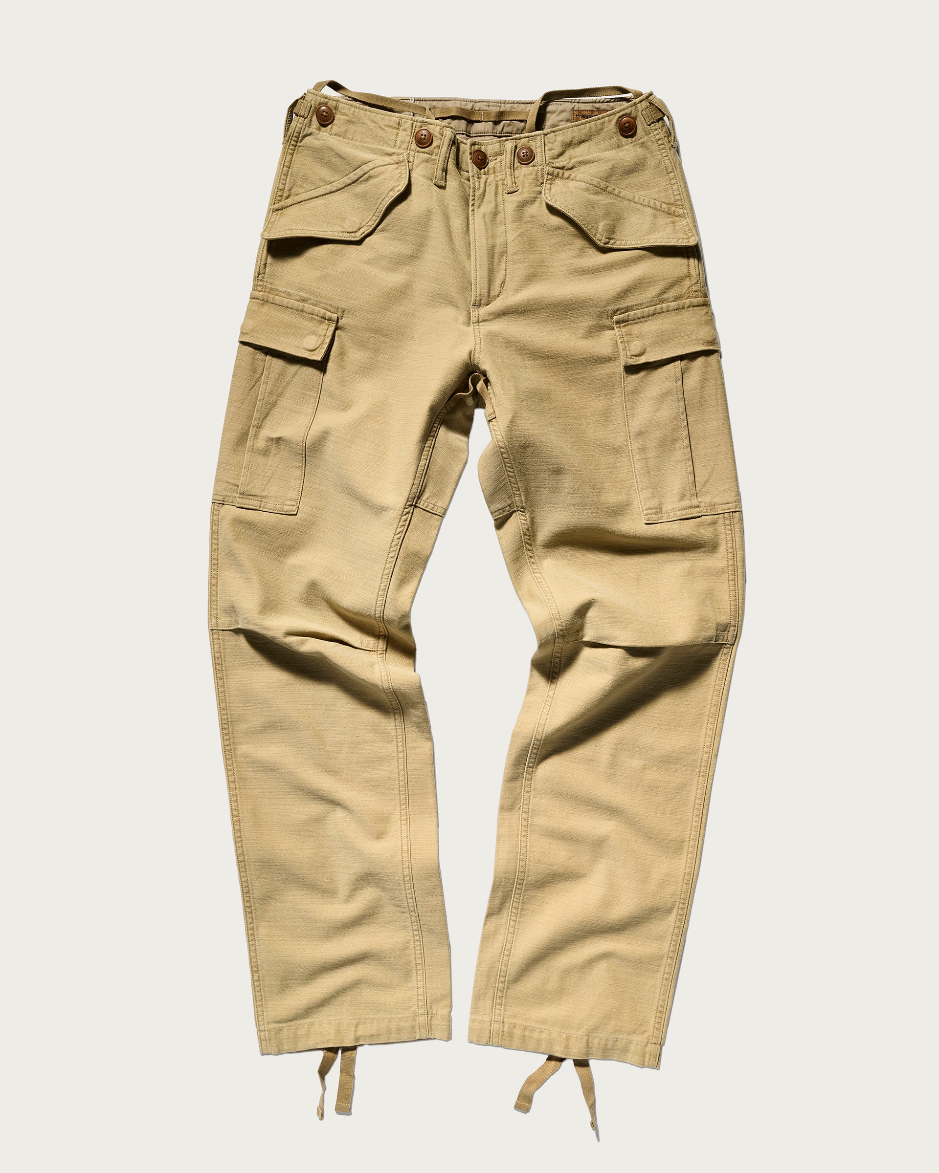 The Brando Cargo in Sand by T7C—cotton-back satin cargo pants with multiple pockets, button and zip closure, and adjustable cuff drawstrings—shown laid flat on a white background.