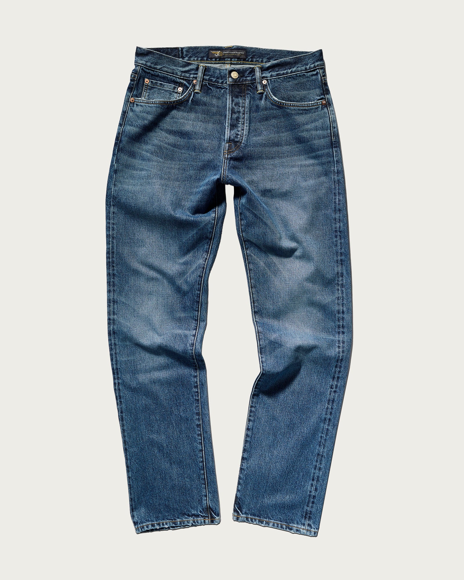 The T7C Charlie Jean in Fuji Medium features classic blue tailoring, a button and zip fly, front and back pockets, and subtle fading on the thighs and knees, displayed flat against a plain light background.