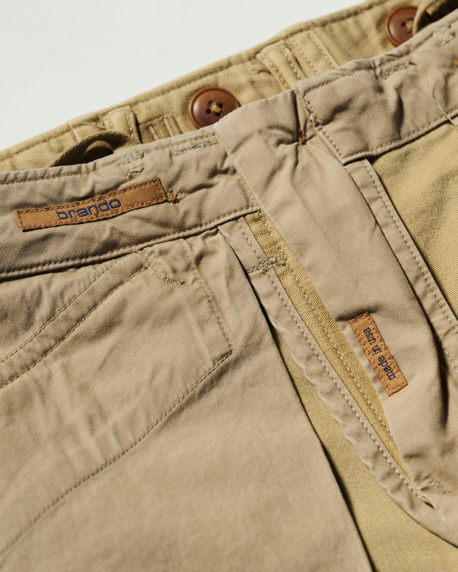 Close-up of The Brando Cargo in Sand by T7C, showcasing brown buttons, visible stitching, belt loops, and two brown tags—one above the pocket with brando and another by the zipper. Crafted using sulphur dyeing for a rich sand finish.