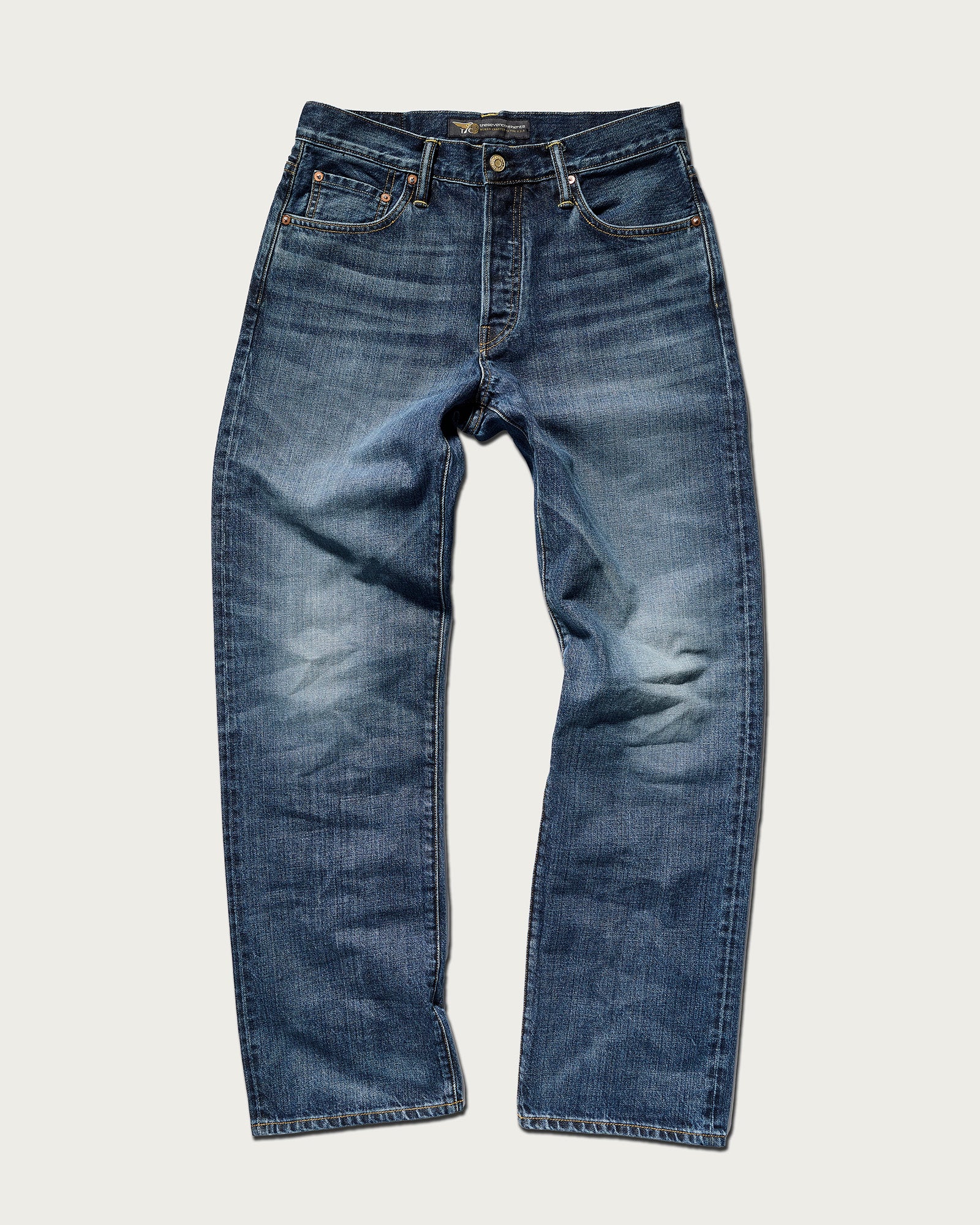 The T7C Jack Jean in Tokyo Medium features blue Japanese denim, a button and zipper closure, subtle fading at the thighs and knees, a classic five-pocket design, and straight legs. Shown laid flat on a plain light background.