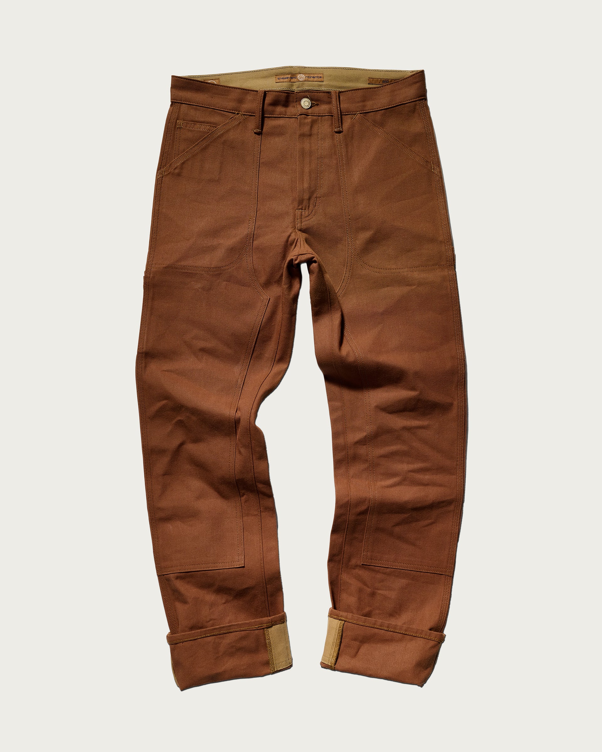 The Sid Pant in Hide Raw by T7C The Seven Continents features visible stitching, large front pockets, and rolled cuffs—crafted for classic workwear style and shown laid flat on a plain white background.