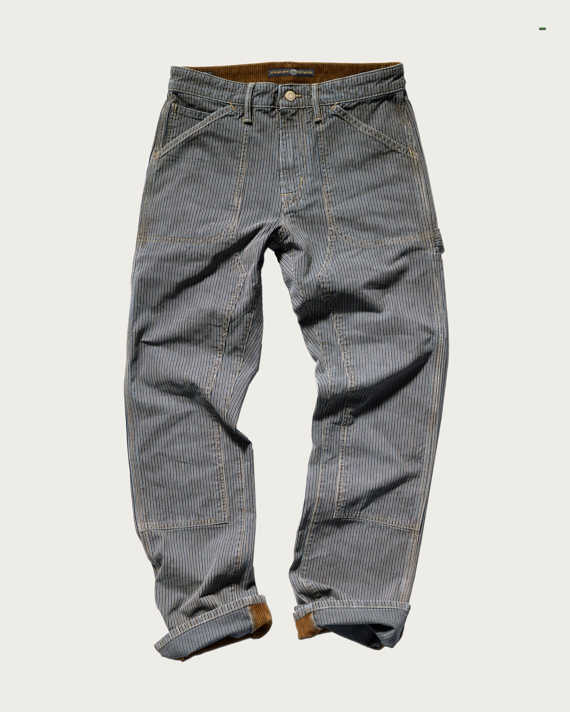The Sid Pant in Indigo Stripe by T7C The Seven Continents features cotton carpenter style with brown cuffs, multiple pockets, and visible stitching, displayed flat on a light background.