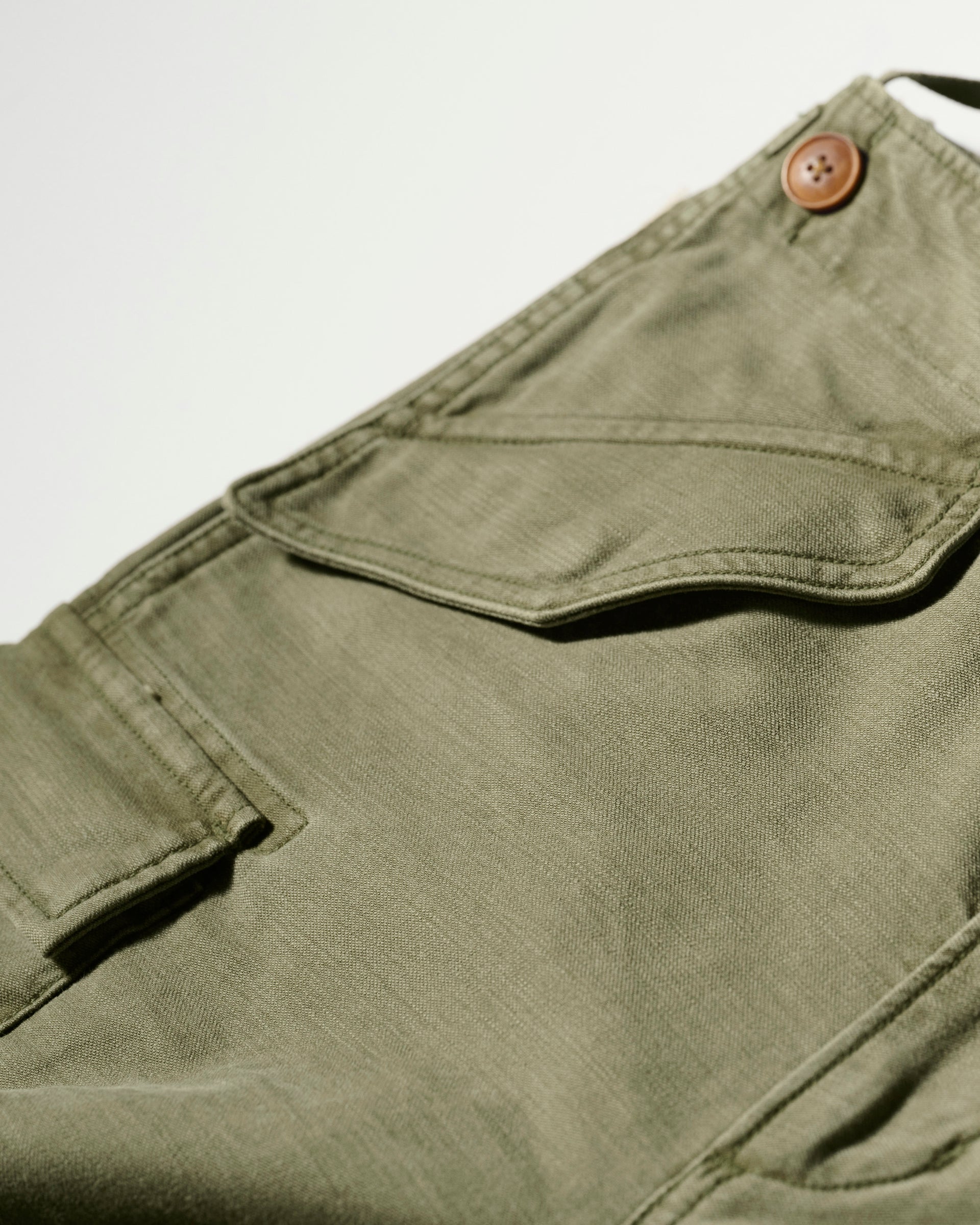 Close-up of The Brando Cargo in Olive Drab by T7C, crafted from cotton-back satin with a flap pocket and brown button. Sulphur dyed for depth, showcased on a white background.