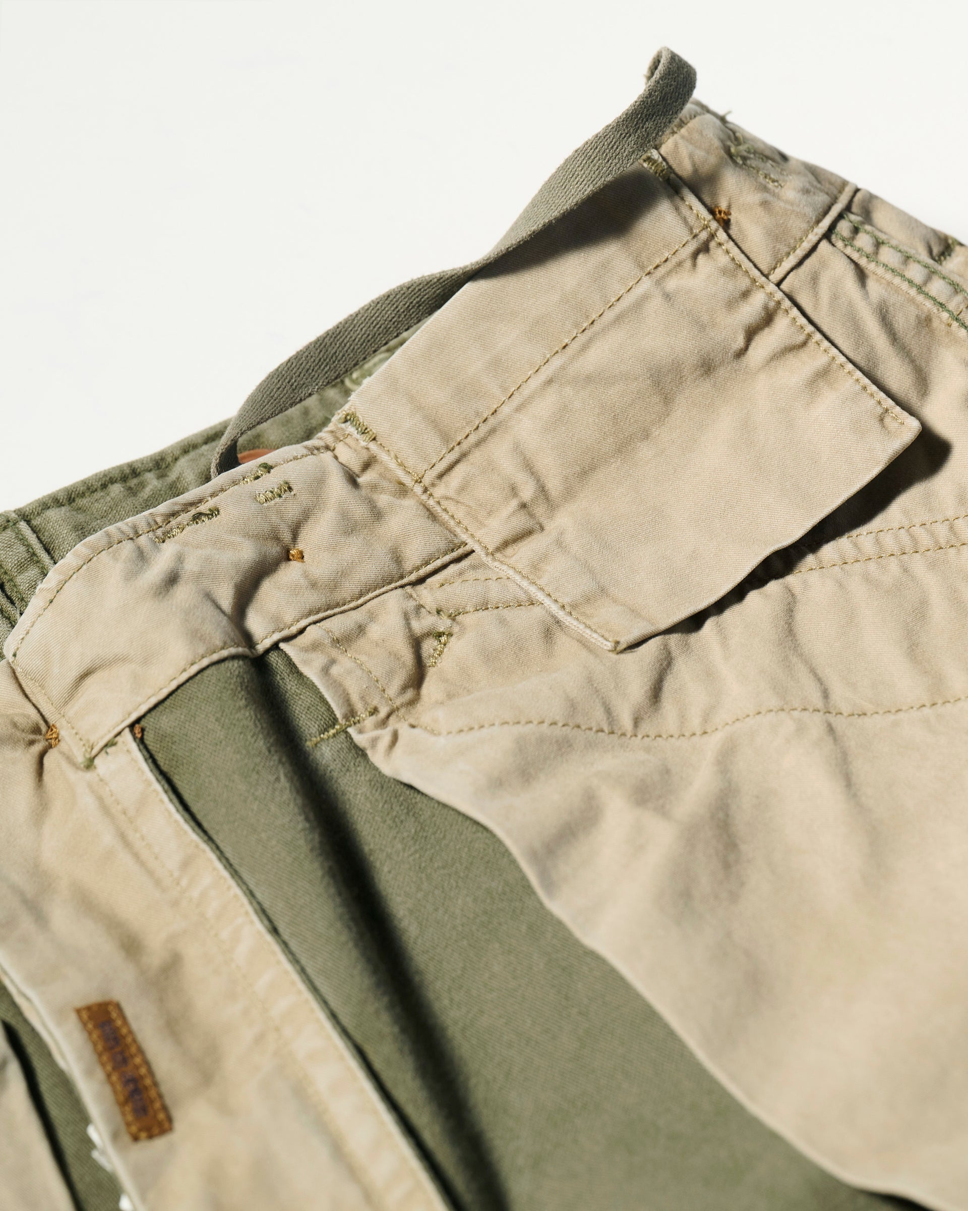 Close-up of the waistband and pocket area of The Brando Cargo in Olive Drab by T7C, showcasing beige and olive green cotton-back satin fabric, visible stitching, and a belt loop.