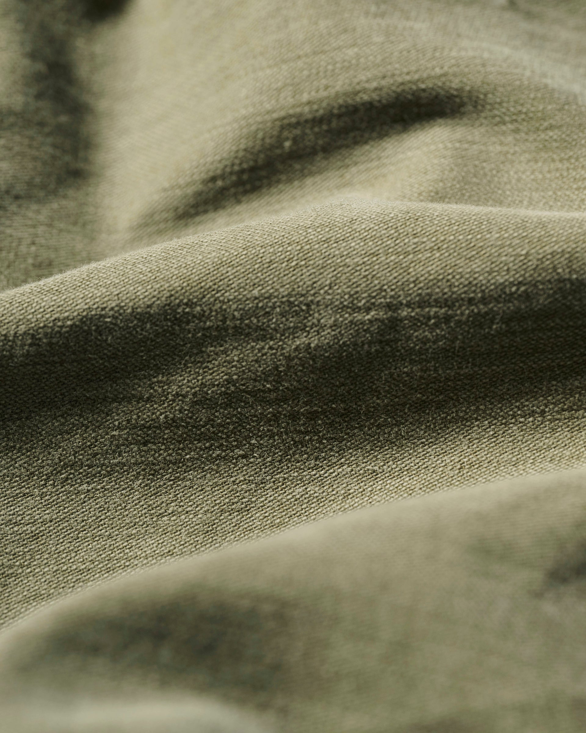 Close-up of The Brando Cargo in Olive Drab by T7C, showcasing its wrinkled, textured cotton-back satin fabric in olive green and beige, with soft shadows highlighting the detailed folds and surface texture.