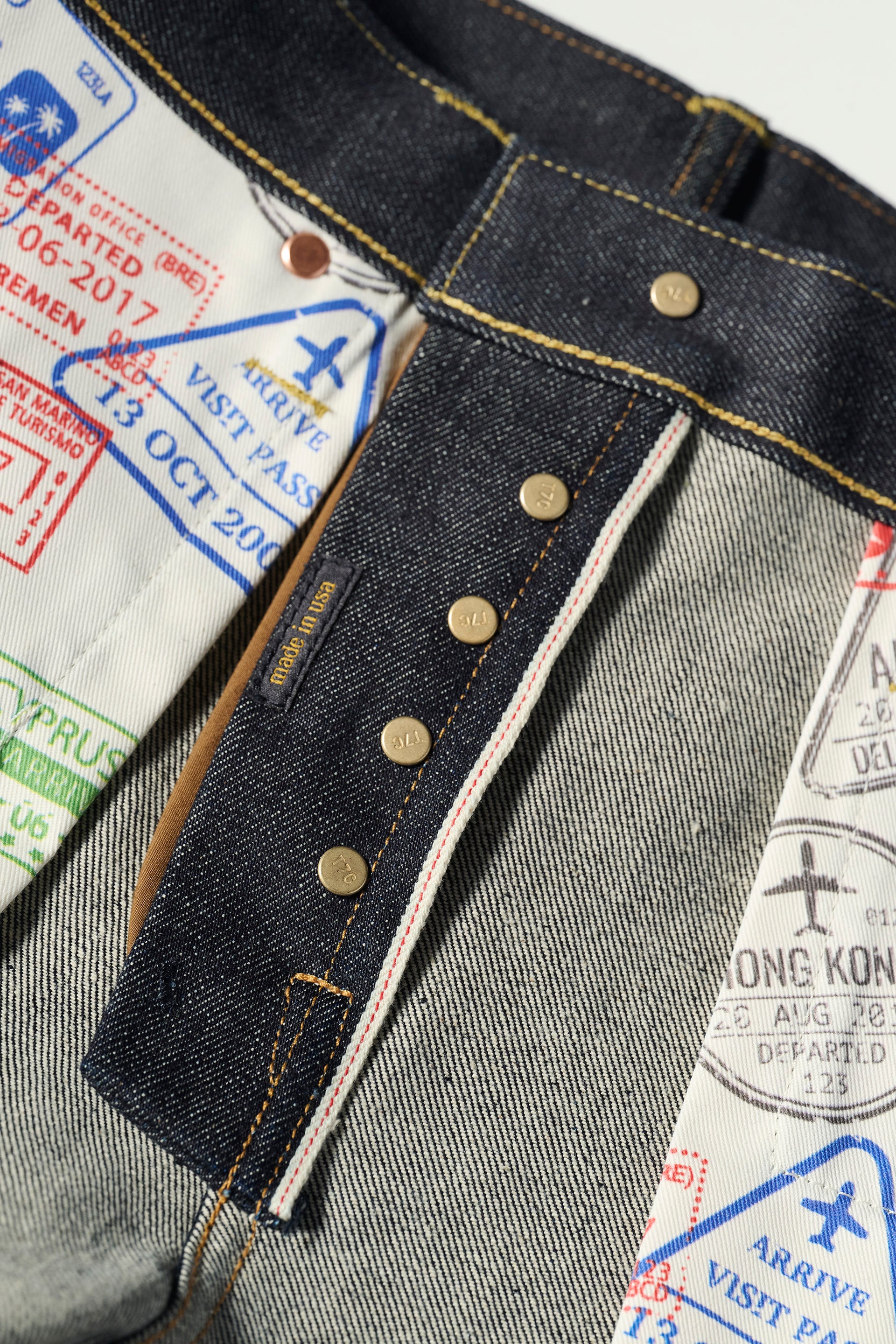Close-up of The Charlie in Yokohama Raw by T7C The Seven Continents—slim fit jeans made from indigo rope-dyed Japanese selvedge denim, with colorful passport stamp lining, brass buttons, and signature yellow stitching.