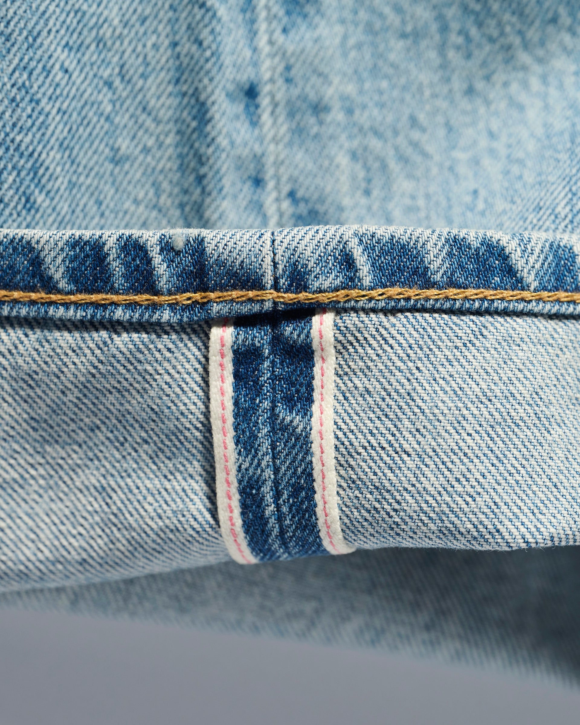 Close-up of light blue Japanese denim from T7C The Seven Continents’ The Charlie Jean in Zuma, showing a selvedge edge with thin red line, white border, and yellow stitching—ideal for slim fit jeans enthusiasts.