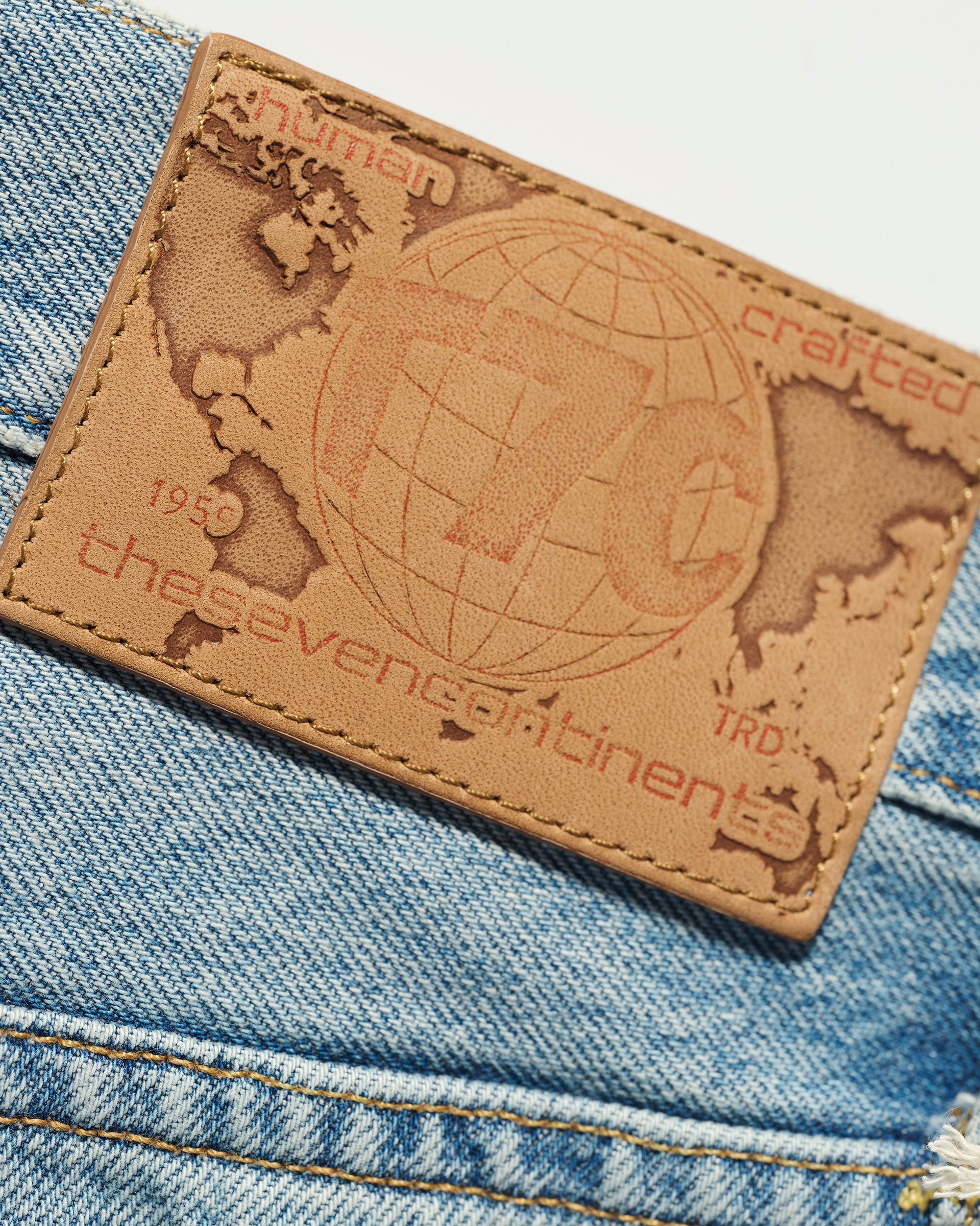 Close-up of a tan leather patch embossed with a world map and T7C branding on The Charlie Jean in Zuma, slim fit blue selvedge denim by T7C The Seven Continents.