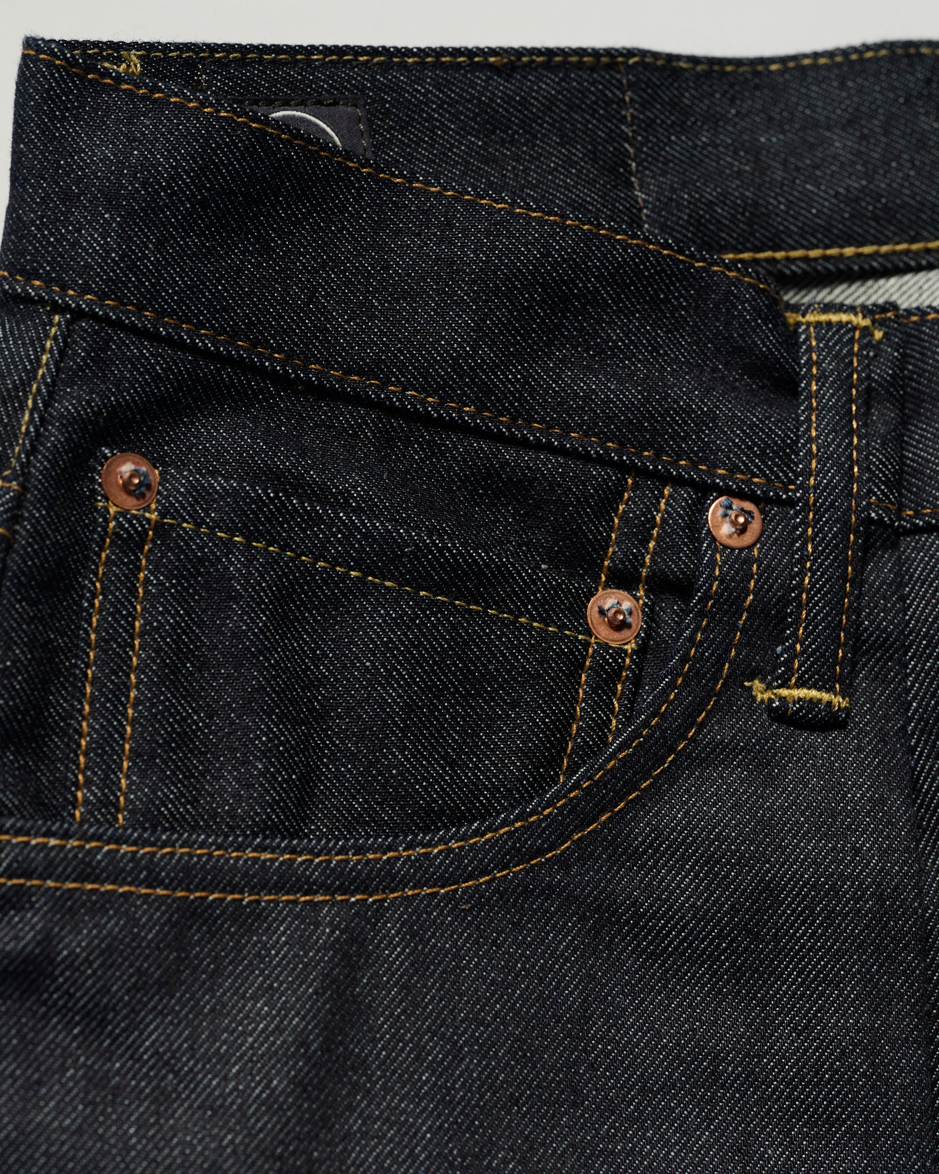 Close-up of the pocket area on T7C The Seven Continents The Cinch Jean in Yokohama Raw, highlighting copper rivets, yellow stitching, small coin pocket, and the textured raw denim of this oversized fit.