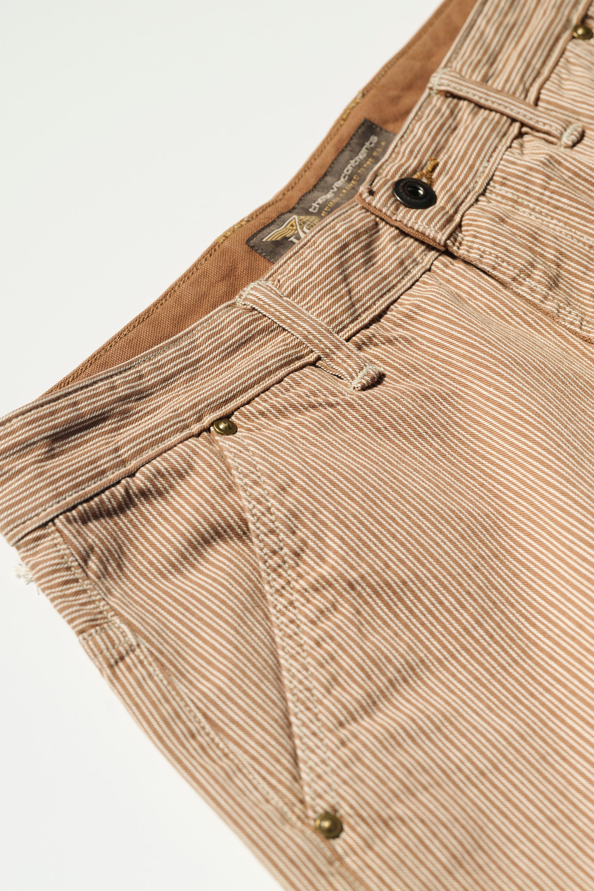 Close-up of The Fred Pant in Camel Stripe by T7C, highlighting the waistband, front pocket, belt loops, brown inner lining, metal rivets, and visible brand label—crafted from premium fabric by a renowned Japanese mill.