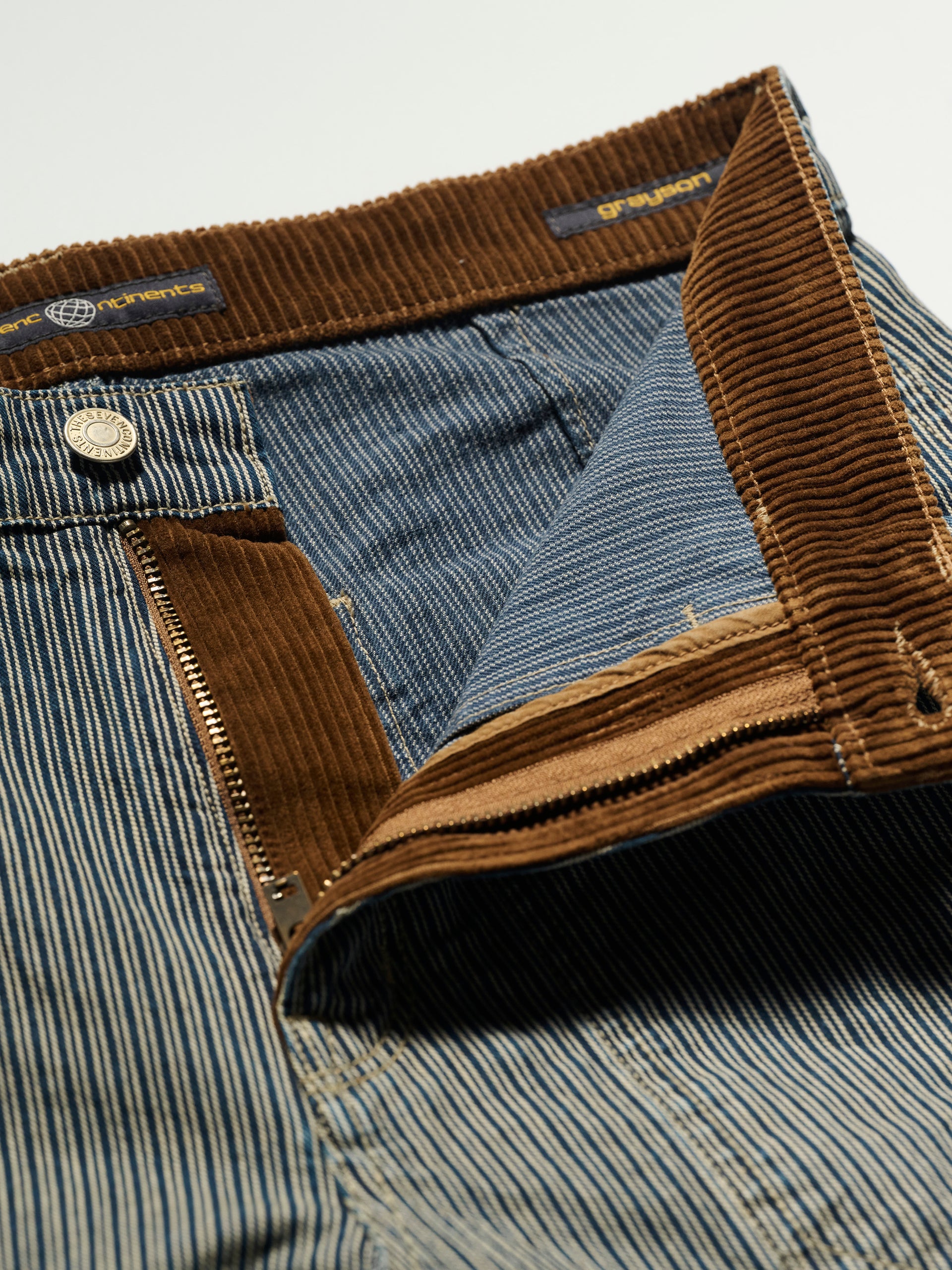 Close-up of The Grayson Pant in Indigo Stripe by T7C The Seven Continents, showcasing the chestnut corduroy waistband and partially open zipper fly with visible corduroy lining and denim interior.