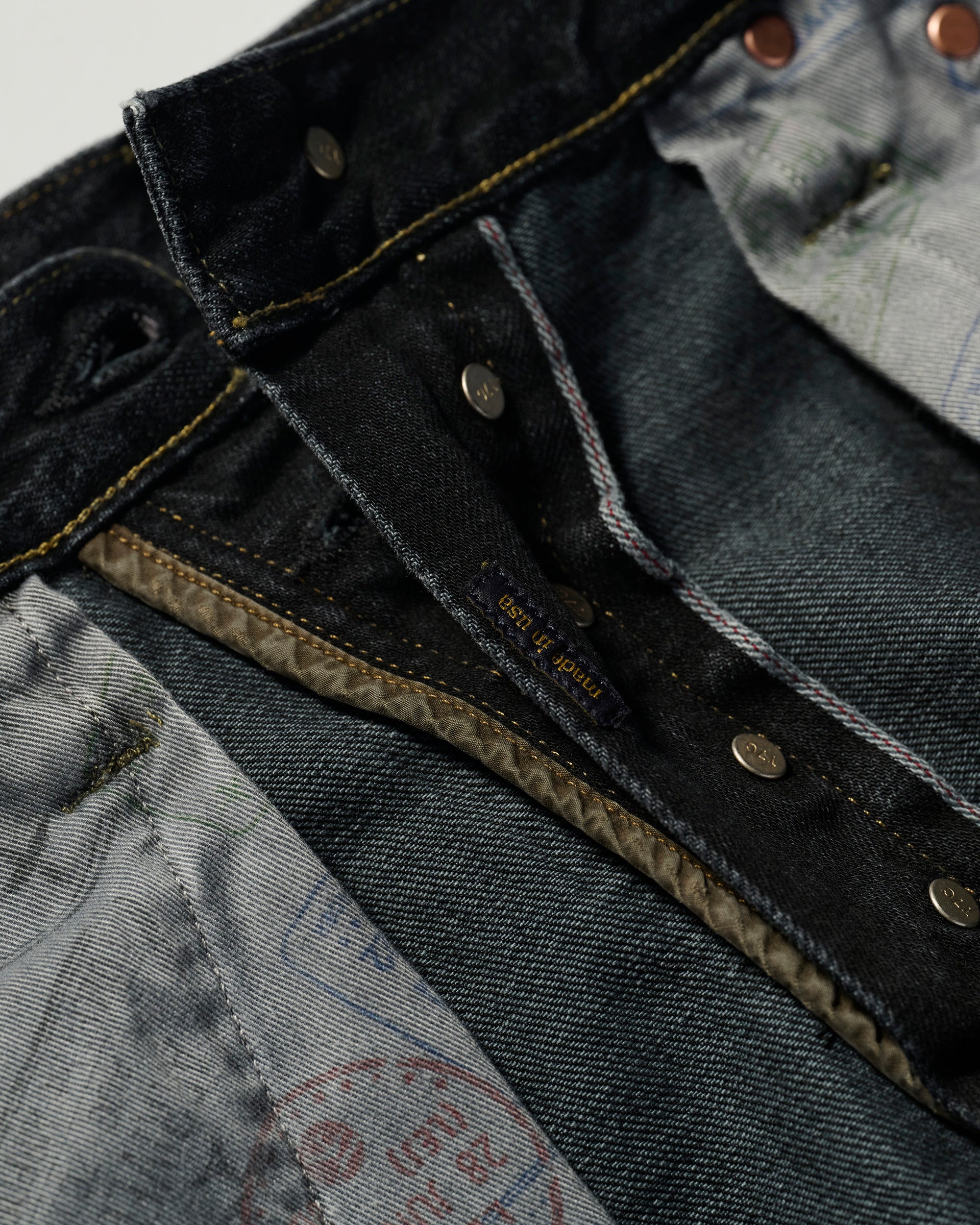 Close-up of the inside waistband and fly area of The Jack Jean In Kobe Black by T7C, highlighting the vintage wash denim fabric, buttons, stitching, and a partial Made in USA label.