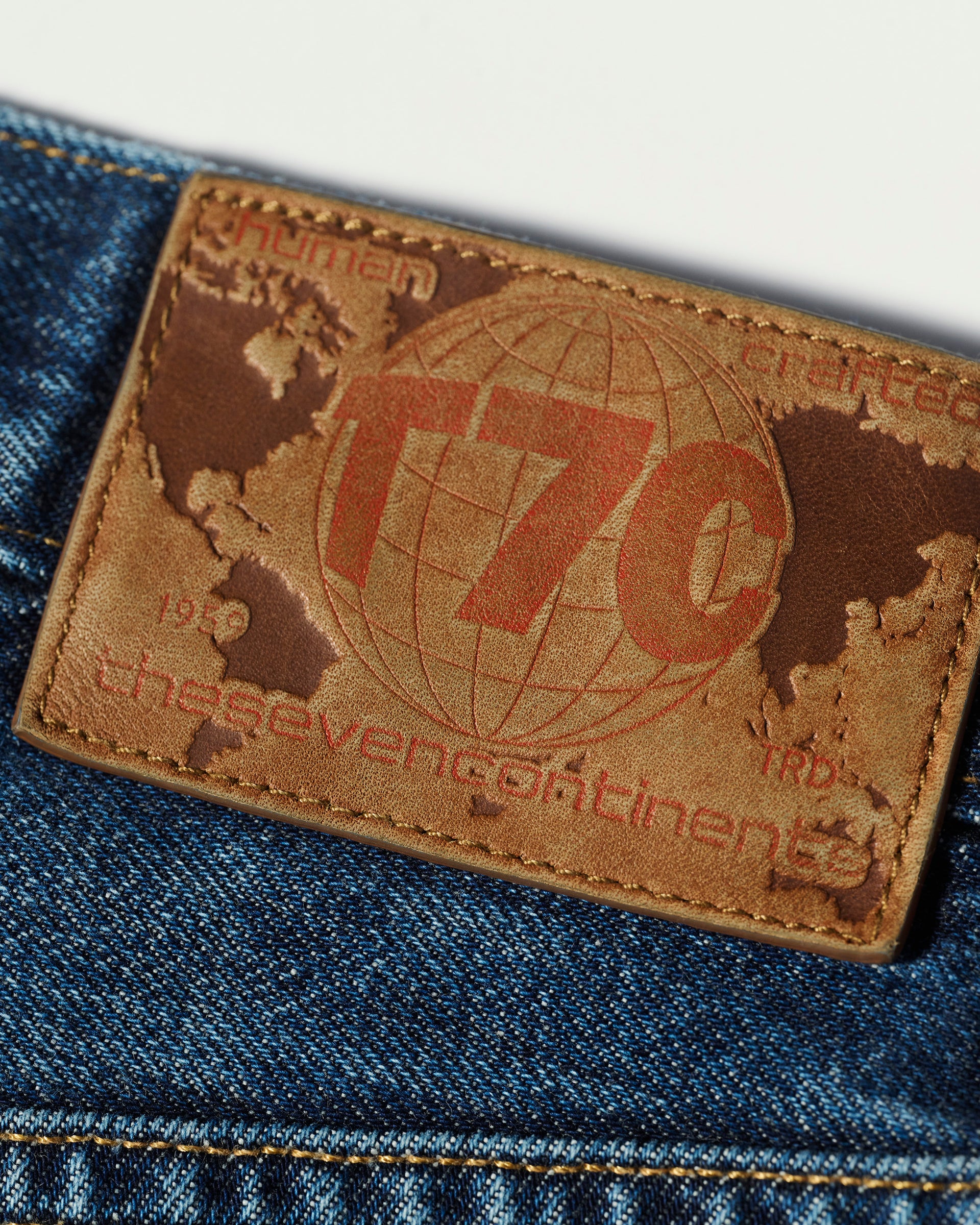 A close-up of the brown leather patch on The Jack Jean in Tokyo Medium by T7C, showing a world map and red lettering of the seven continents, set against rich vintage Japanese denim.