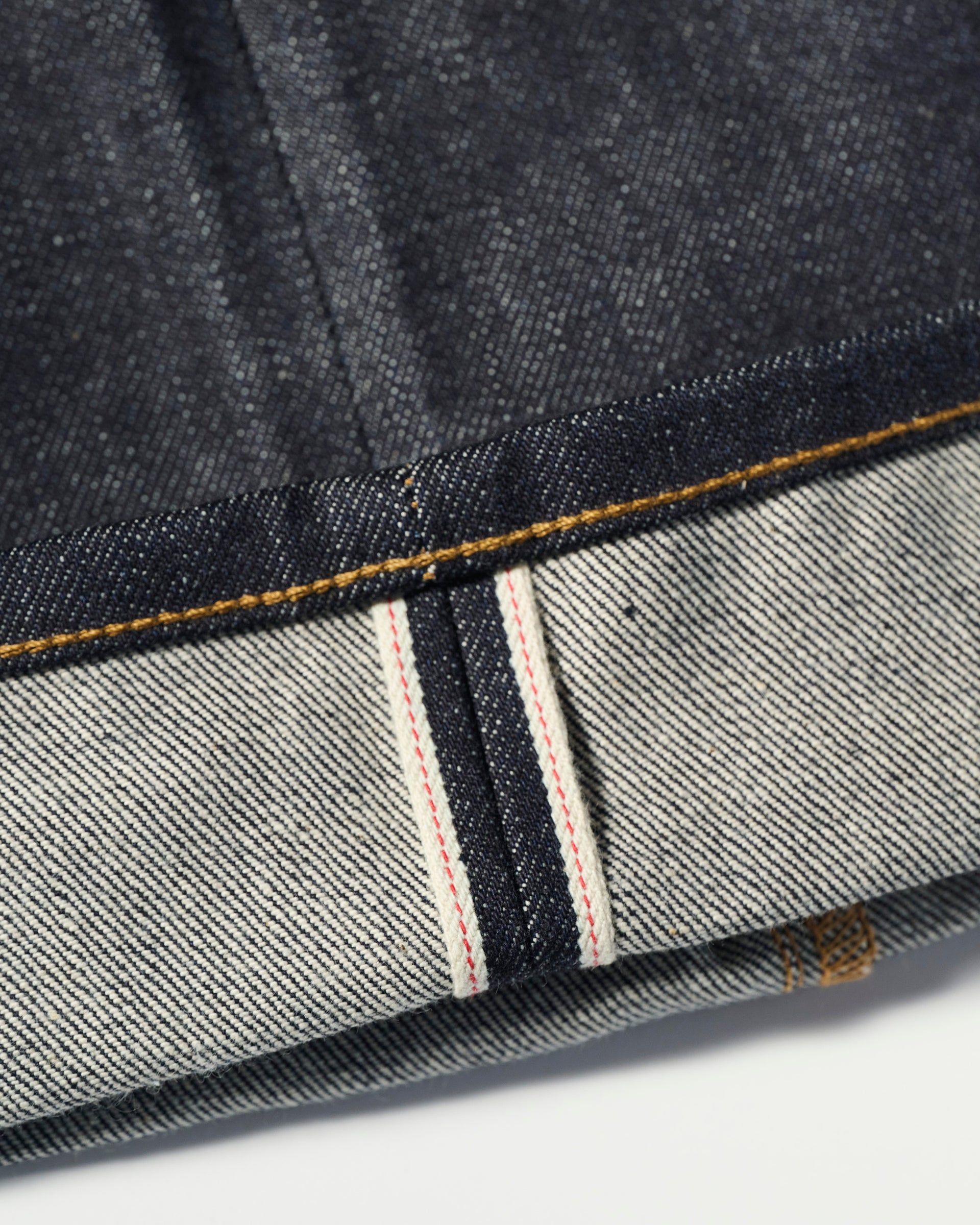 Close-up of the cuff on The Jack Jean In Yokohama Raw by T7C The Seven Continents, highlighting the white selvedge edge with red thread, rope-dyed indigo Japanese denim, diagonal weave, and yellow stitching.
