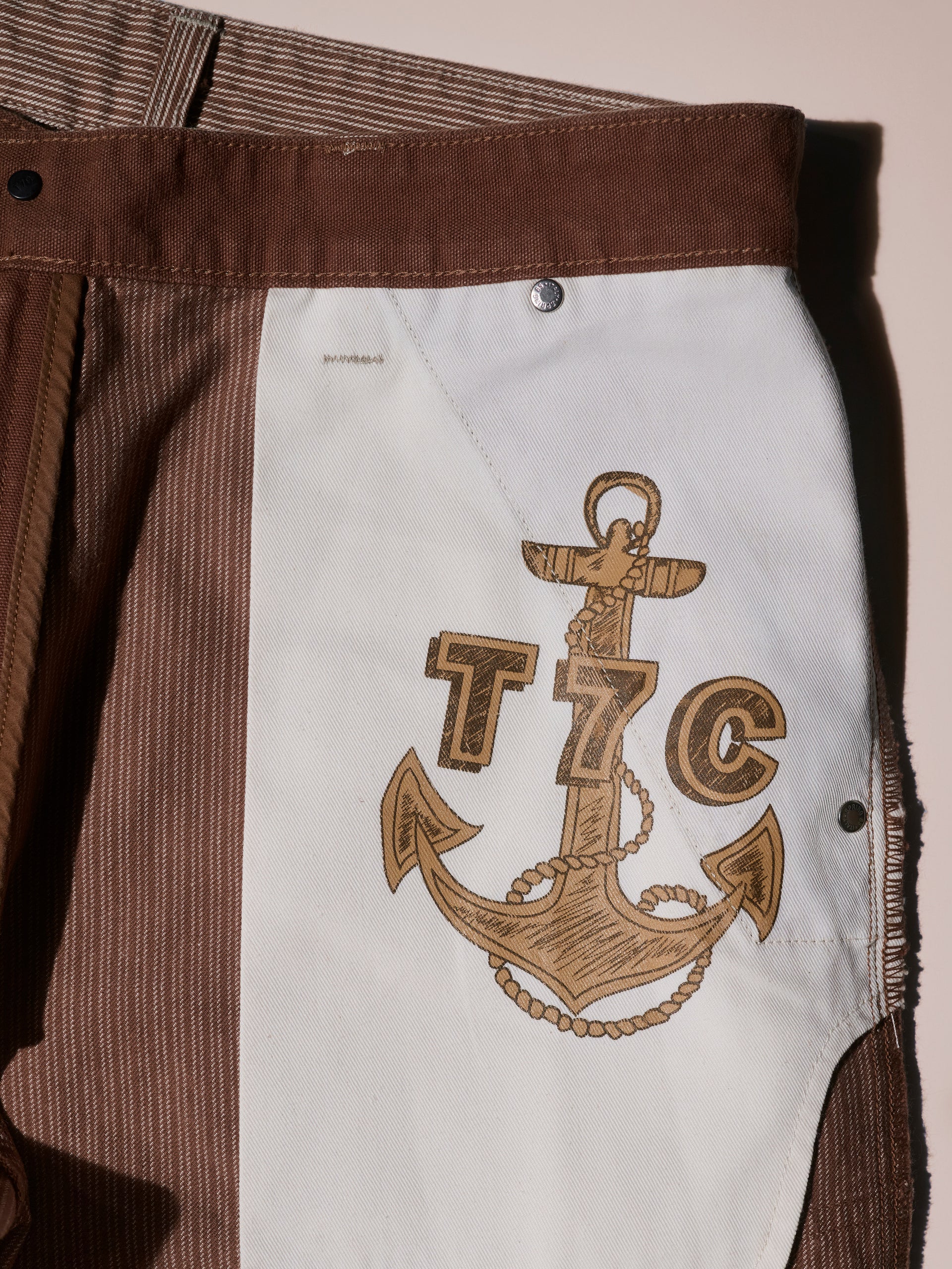 Close-up of The Fred Pant in Camel Stripe by T7C, highlighting the white interior panel featuring a bold anchor and rope graphic alongside the T7C logo.