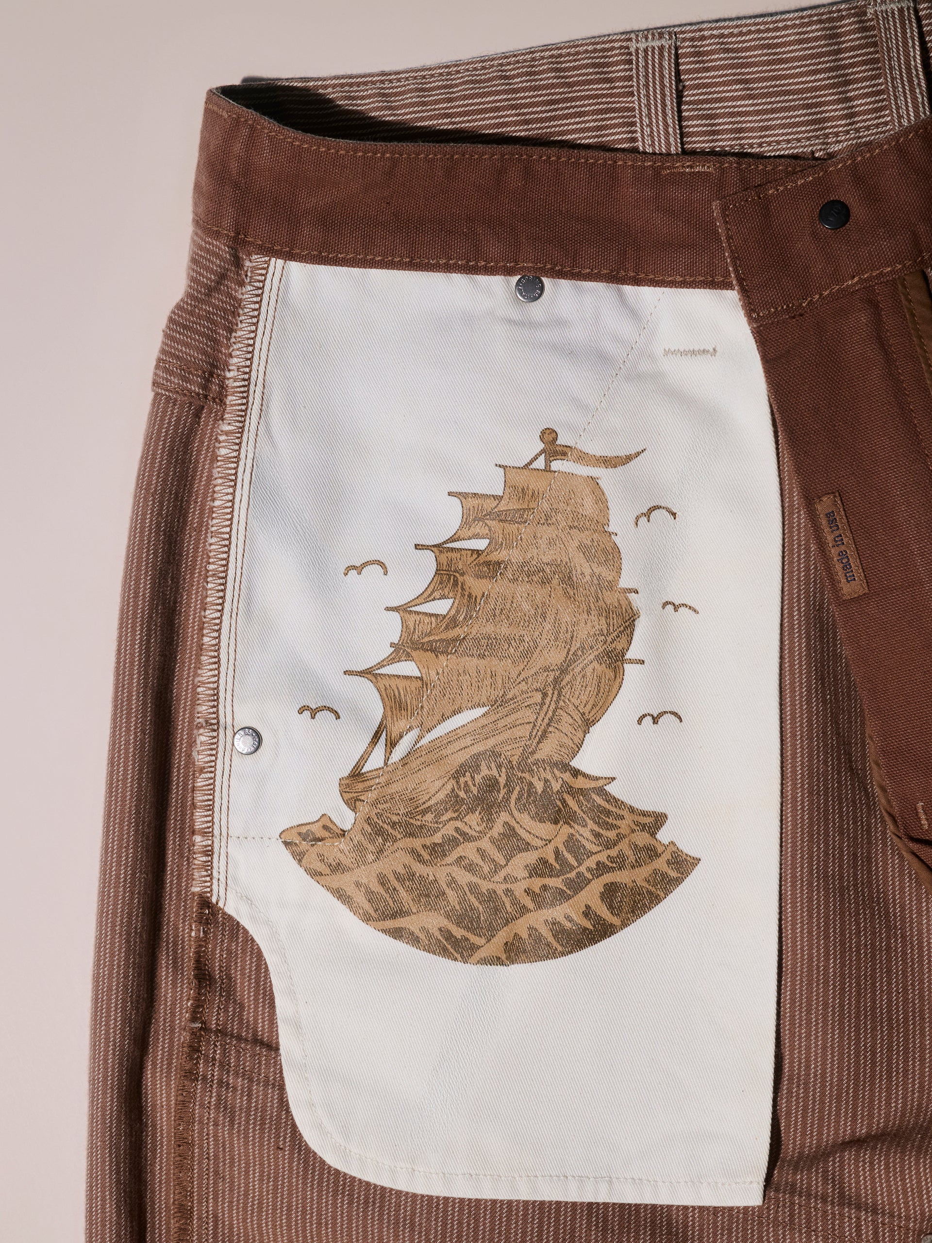 Close-up of the inside pocket of T7Cs The Fred Pant in Camel Stripe, featuring a printed illustration of a tall sailing ship on waves with birds flying above.