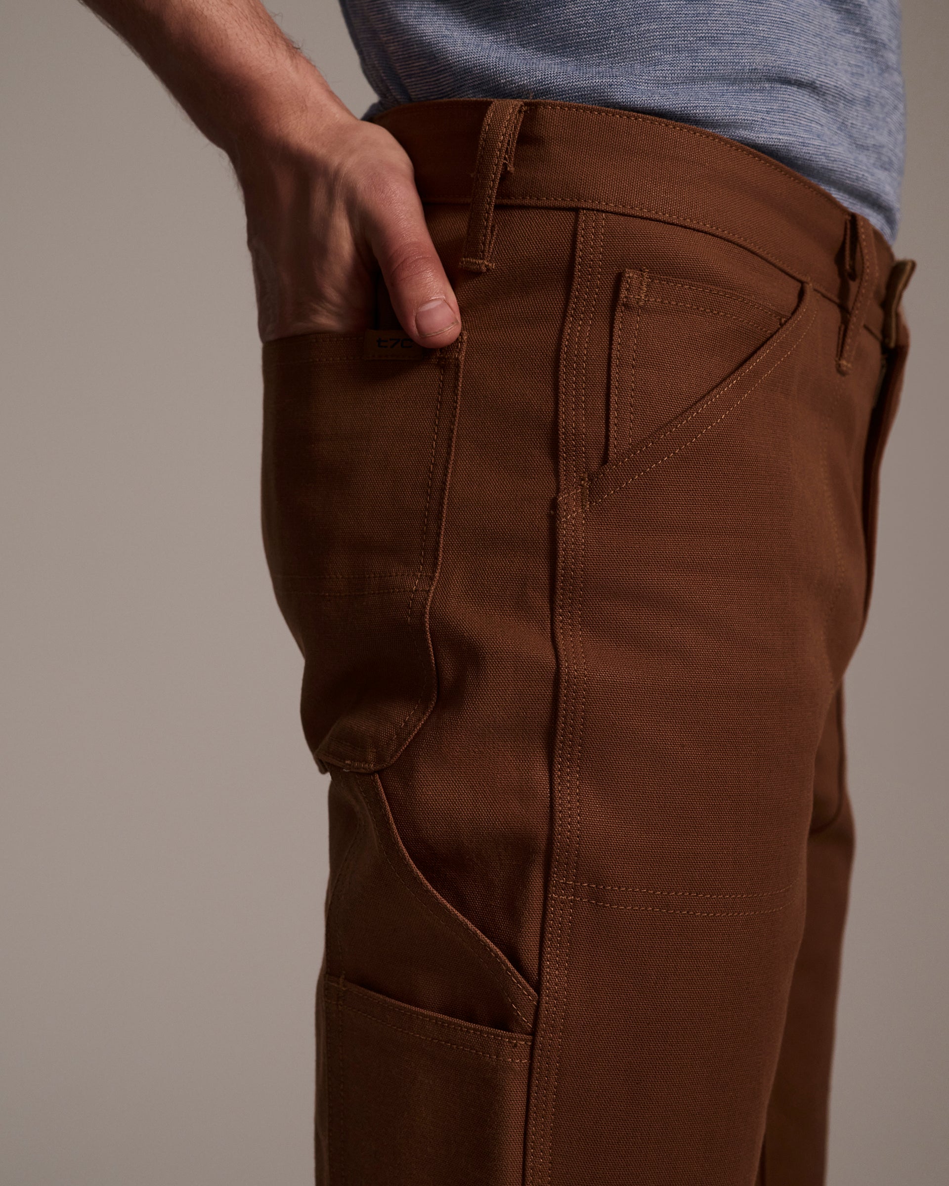 Someone stands with one hand in their pocket, wearing T7C The Seven Continents’ The Sid Pant in Hide Raw, shown from the waist down against a neutral background.