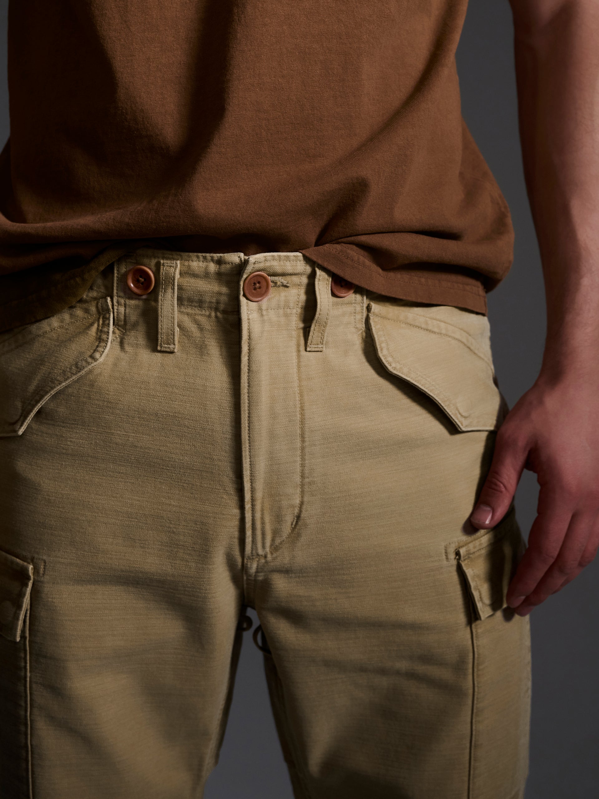 A person wears T7C’s The Brando Cargo in Sand, light beige cotton-back satin pants, paired with a brown t-shirt. One hand rests near their thigh as the cropped image highlights the waist and upper legs.