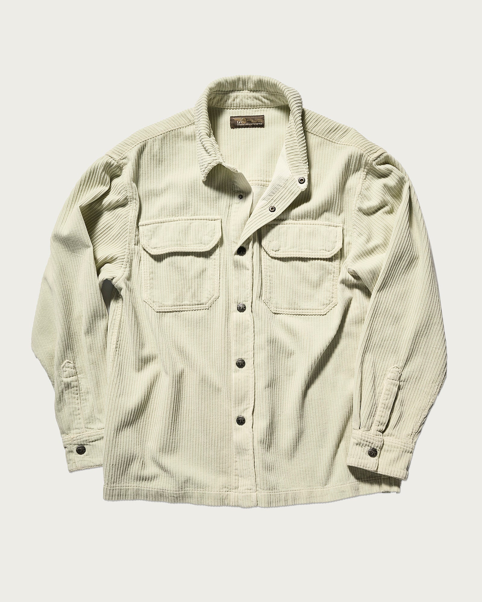 The Aiden Overshirt in Cream by T7C is a cream-colored Japanese corduroy overshirt with two chest pockets, black buttons, and long sleeves, shown on a plain white background.