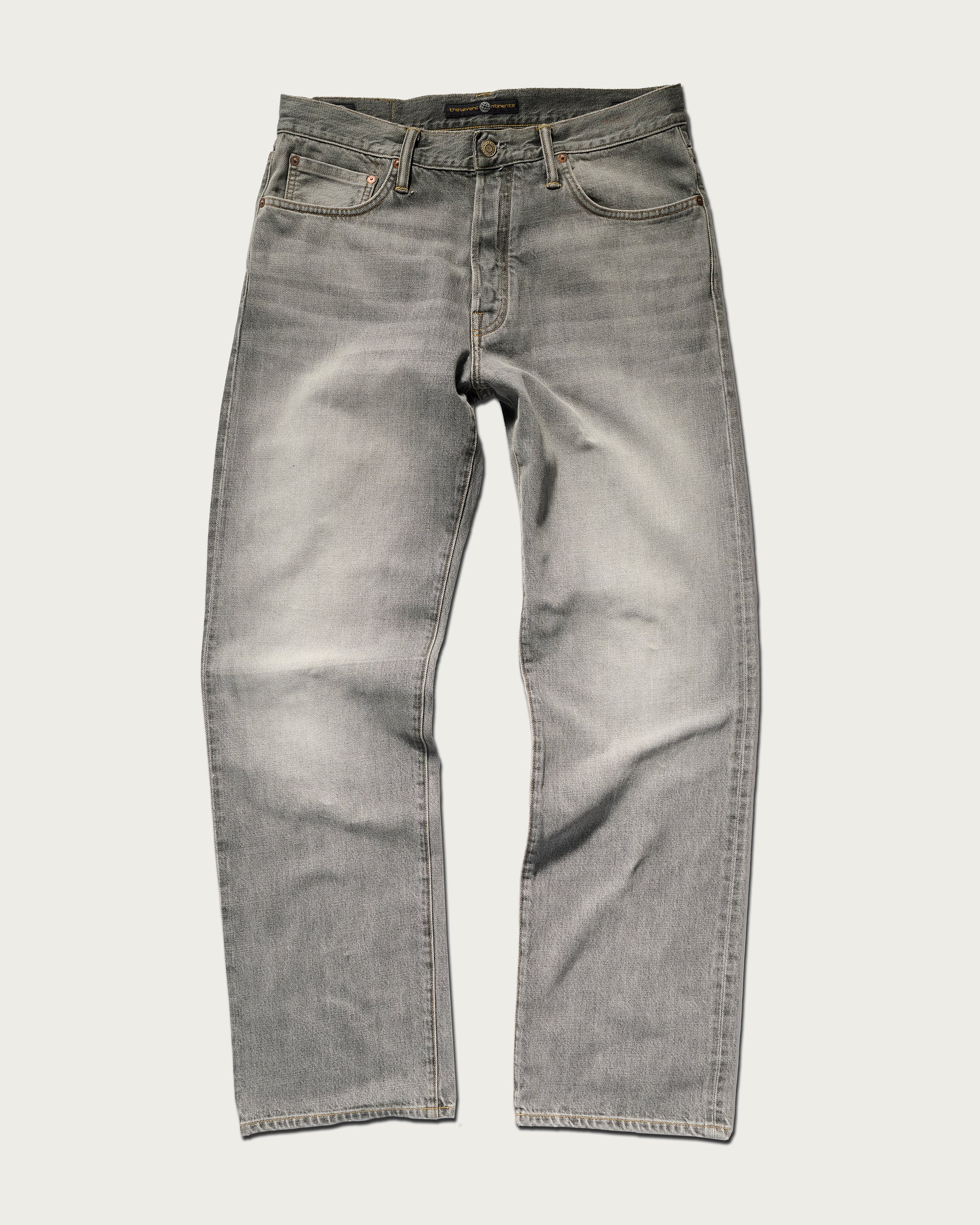 The Jack Jean in Cloud by T7C features light gray, straight-leg jeans made from organic Turkish cotton with five-pocket styling, belt loops, and a button fly, shown flat on a white background.