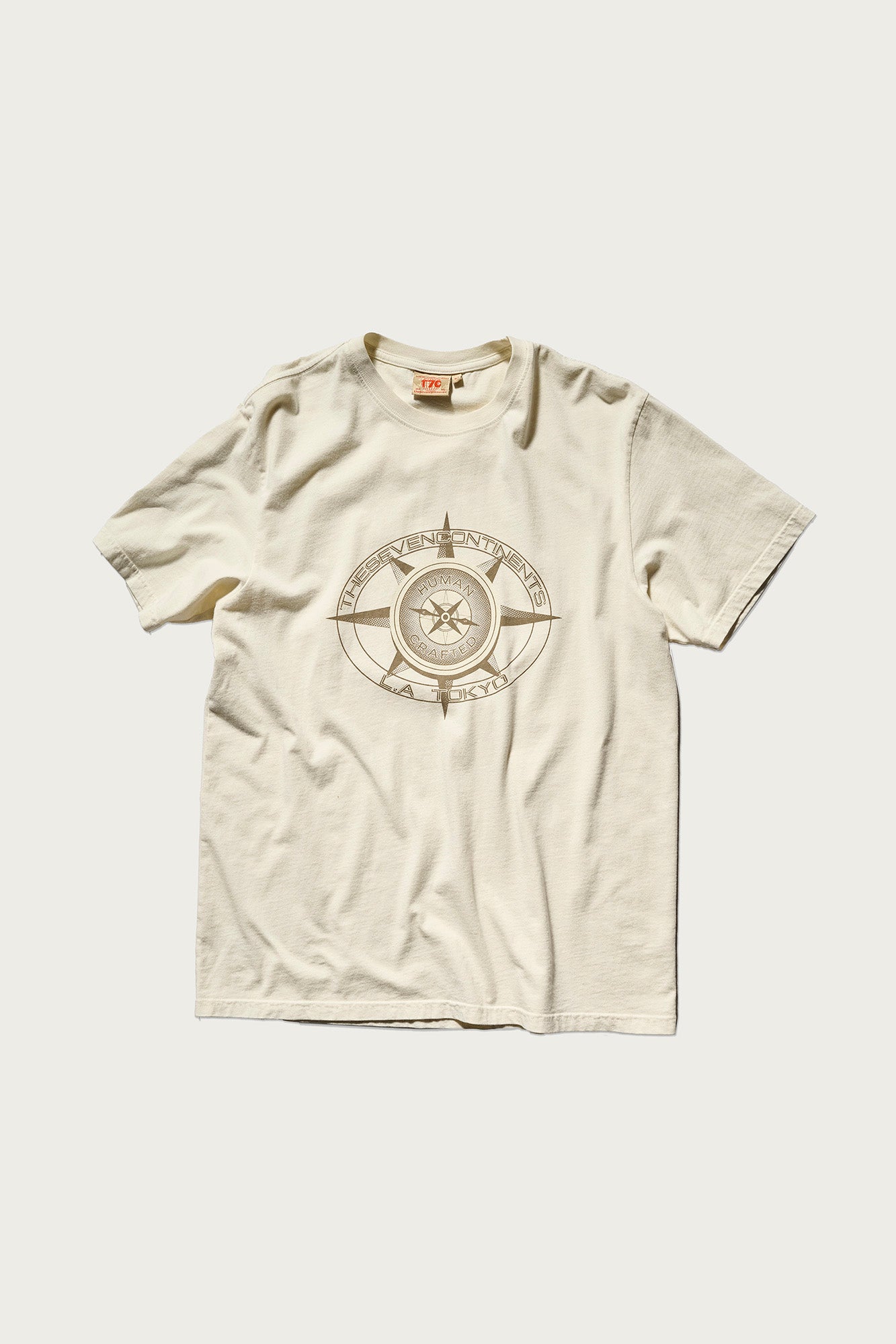The PRE-ORDER: THE KNOXS TEE WITH MERIDIAN PRINT by T7C is a cream short-sleeve round-neck shirt featuring a bold, circular compass-inspired graphic with a star at the center of the chest.