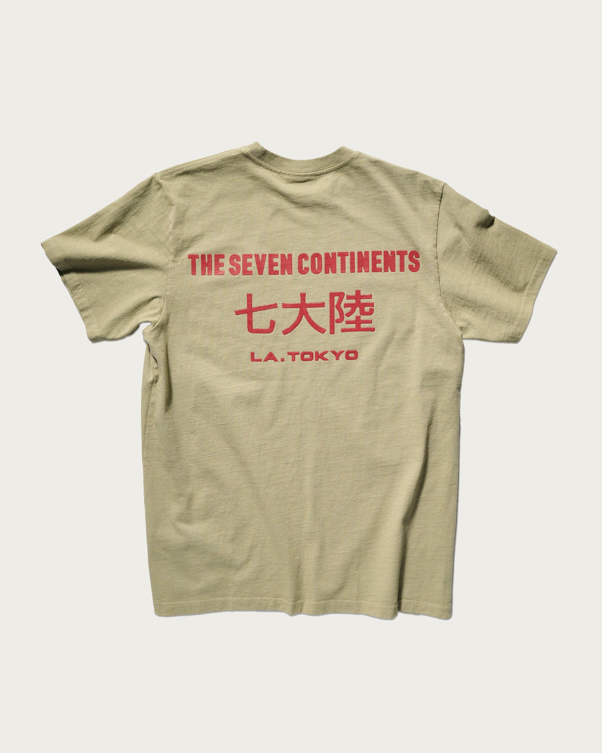The Timo Tee in Taupe by T7C The Seven Continents features a puff screen printed logo, red THE SEVEN CONTINENTS text, Japanese characters, and “L.A. TOKYO” on the back. Shirt is gently laundered and displayed flat on a light background.