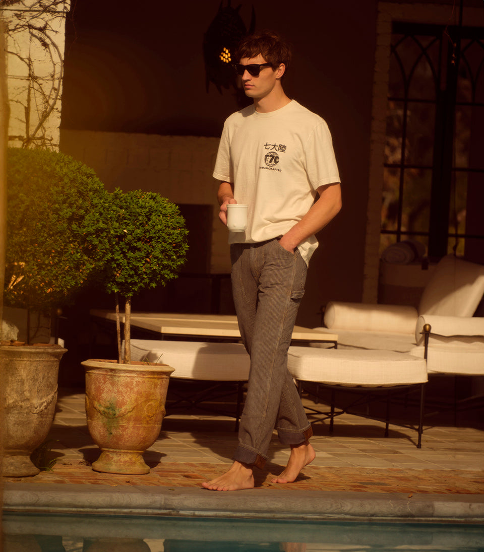 A male model wearing a t-shirt and rail road striped pants walking by a pool