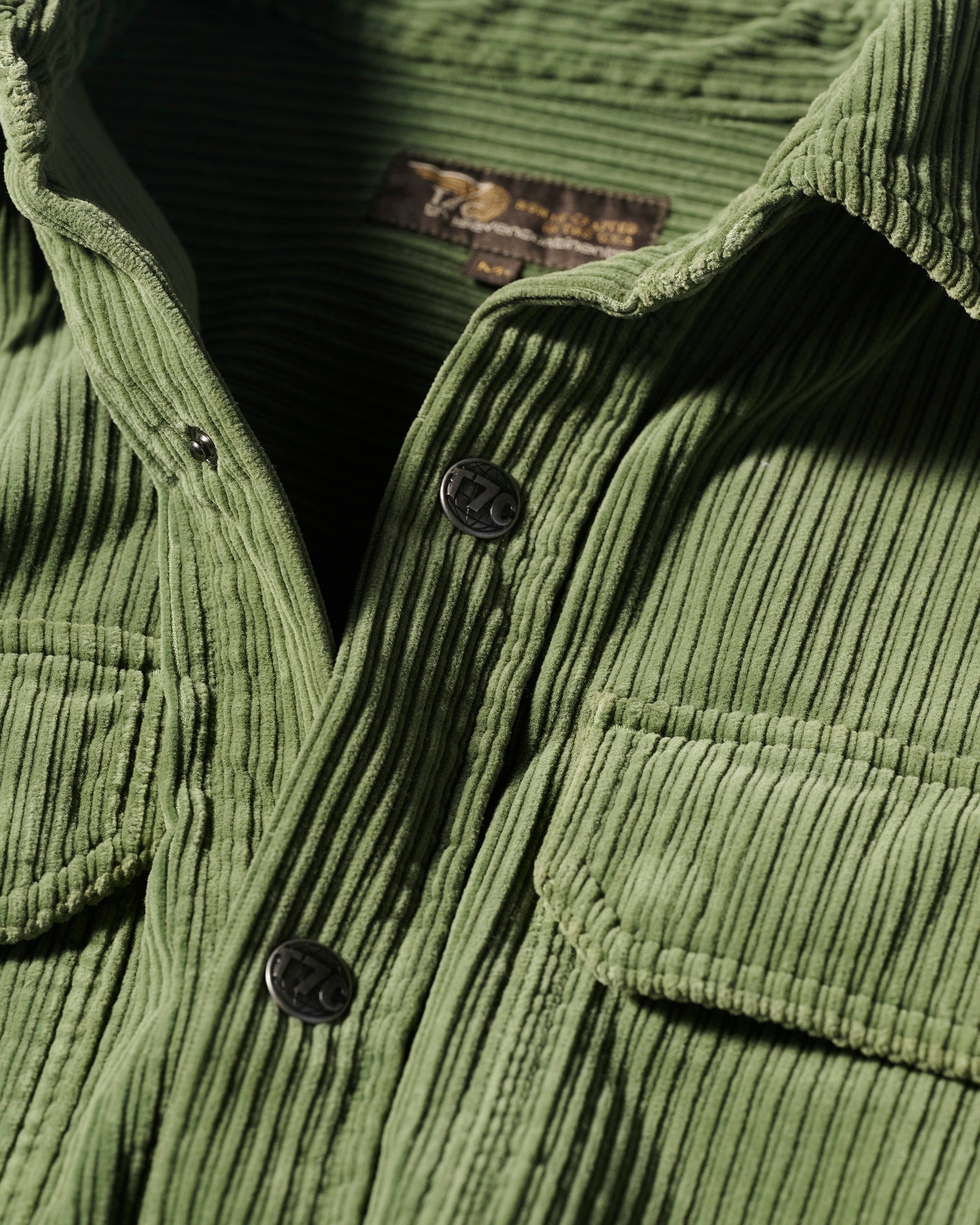Close-up of The Aiden Overshirt in Green by T7C, featuring black buttons, a visible collar, textured corduroy ridges, and a single flap pocket.