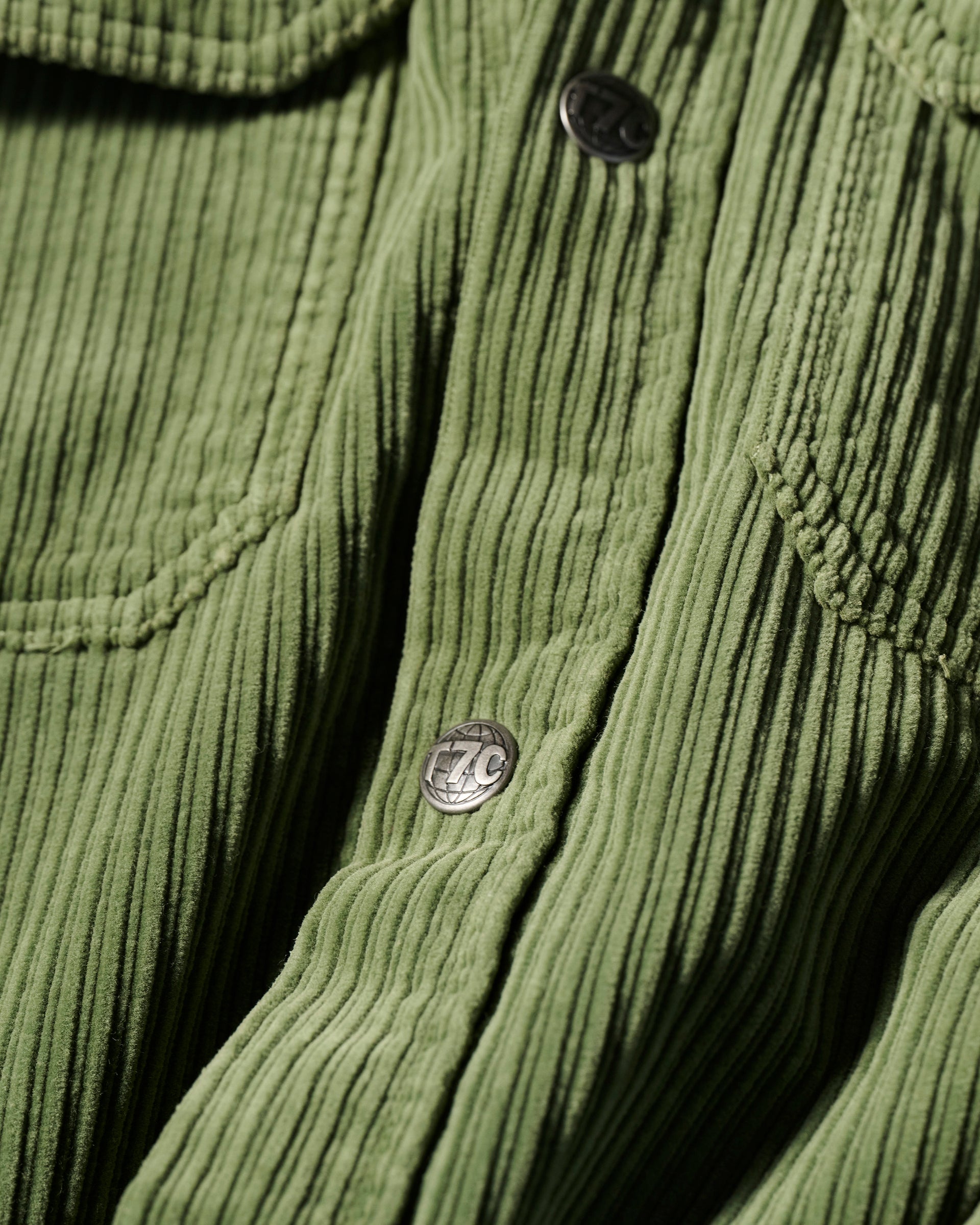 Close-up of The Aiden Overshirt in Green by T7C, featuring textured corduroy with vertical ridges, a flap pocket, and metal snap buttons engraved with 7C.