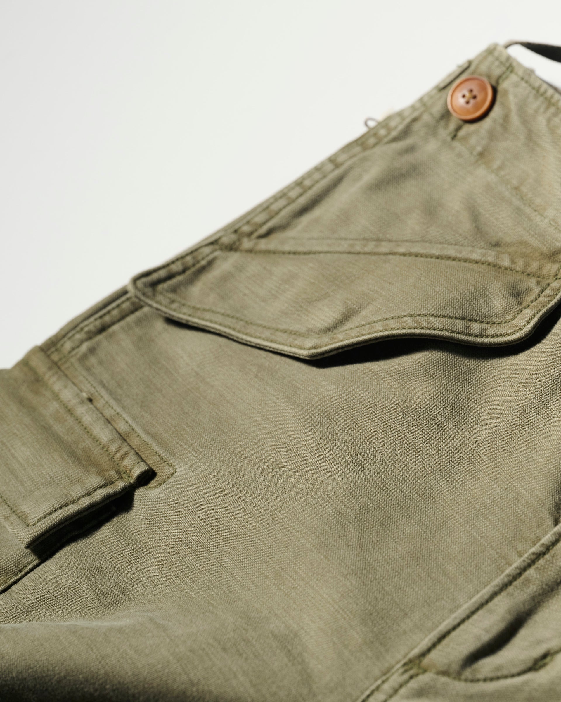Close-up of The Brando Cargo in Olive Drab by T7C, crafted from cotton-back satin with a flap pocket and brown button. Sulphur dyed for depth, showcased on a white background.