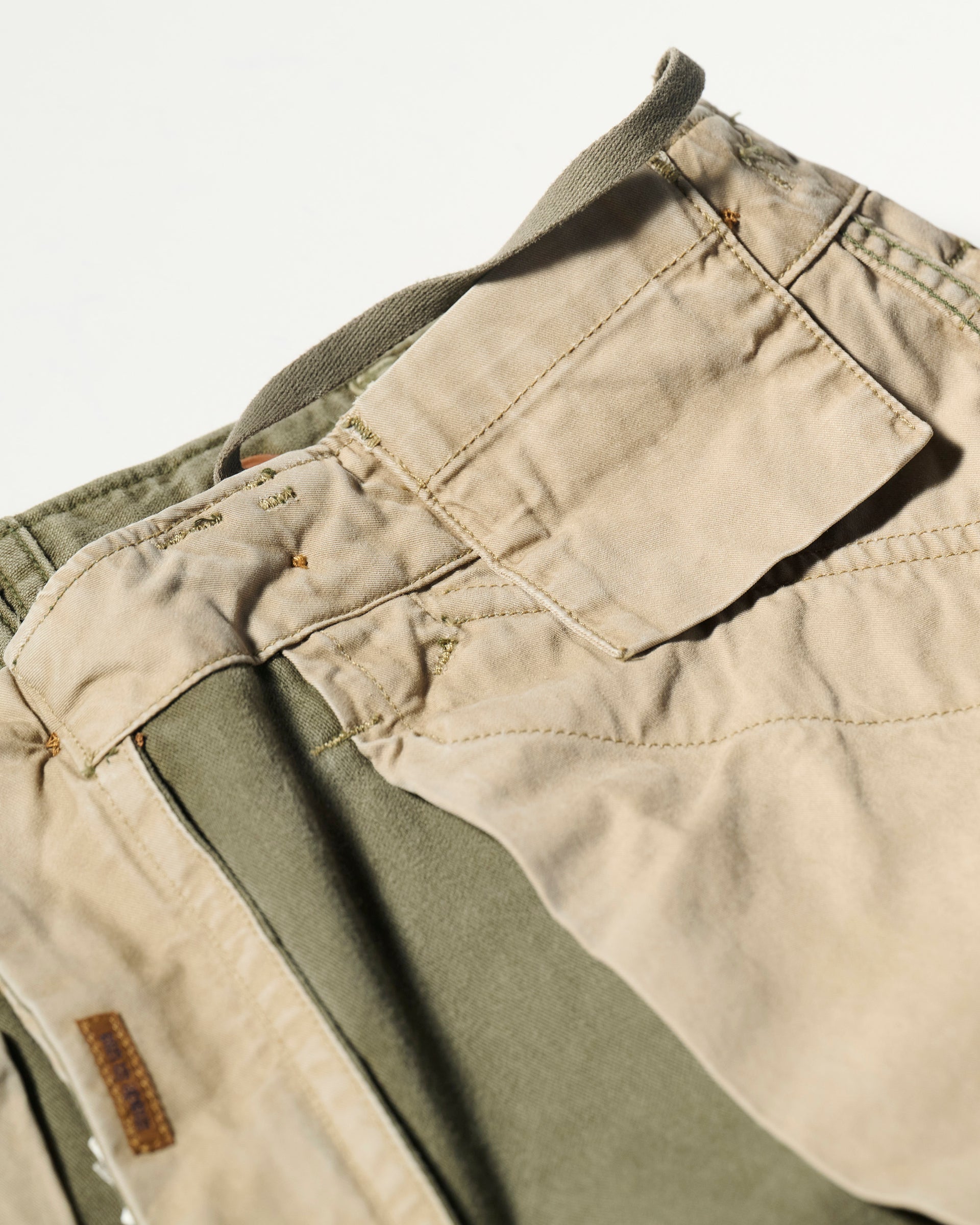 Close-up of the waistband and pocket area of The Brando Cargo in Olive Drab by T7C, showcasing beige and olive green cotton-back satin fabric, visible stitching, and a belt loop.