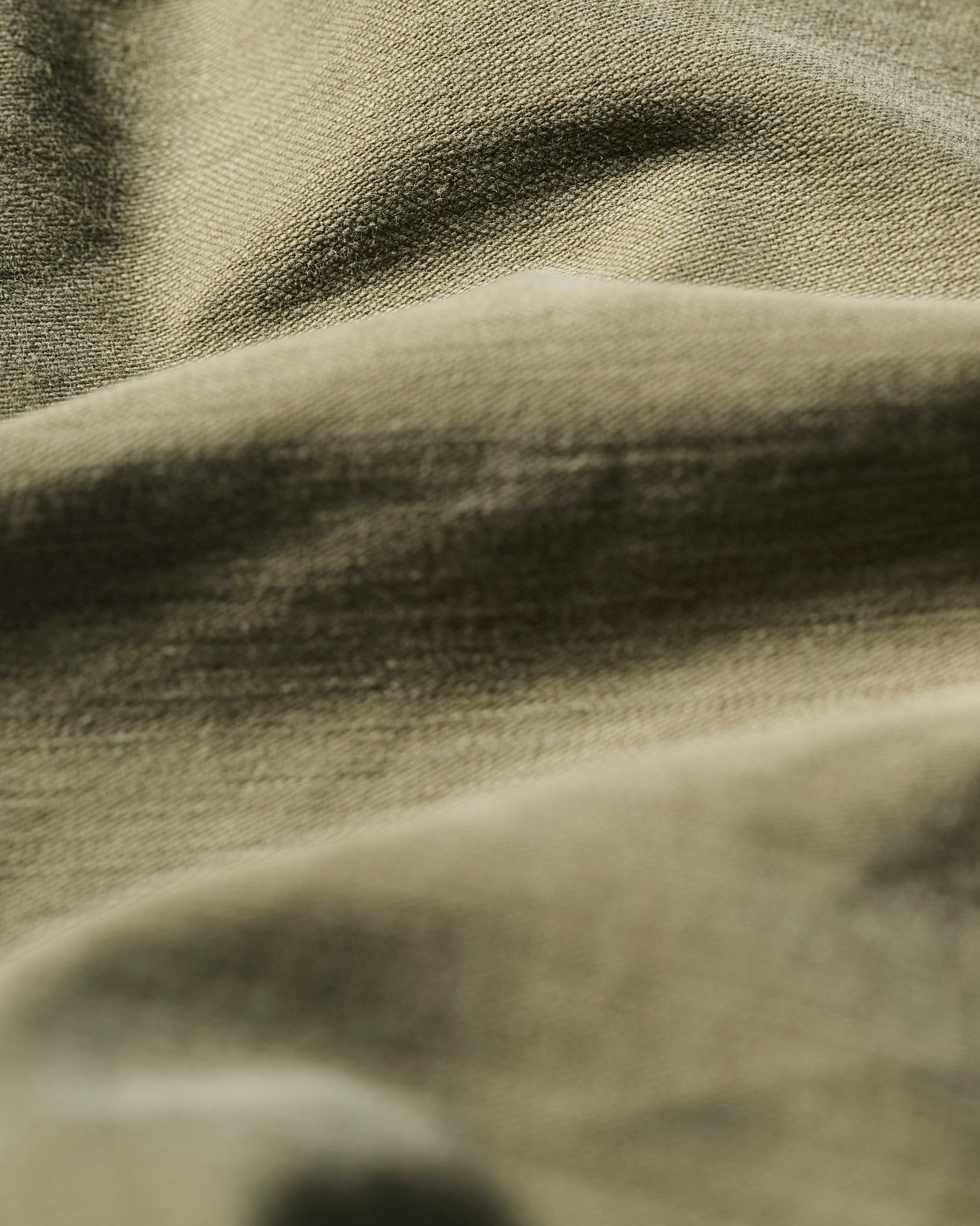 Close-up of The Brando Cargo in Olive Drab by T7C, showcasing its wrinkled, textured cotton-back satin fabric in olive green and beige, with soft shadows highlighting the detailed folds and surface texture.
