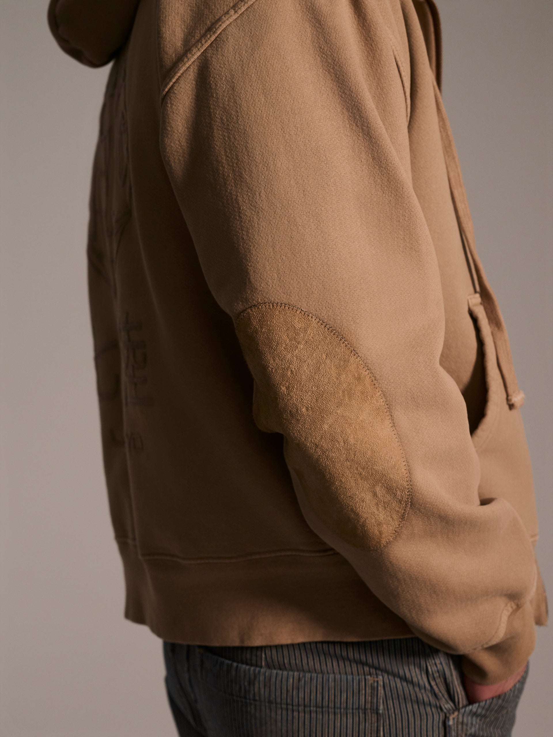 A detail image of a suede patch on a tan hoodie