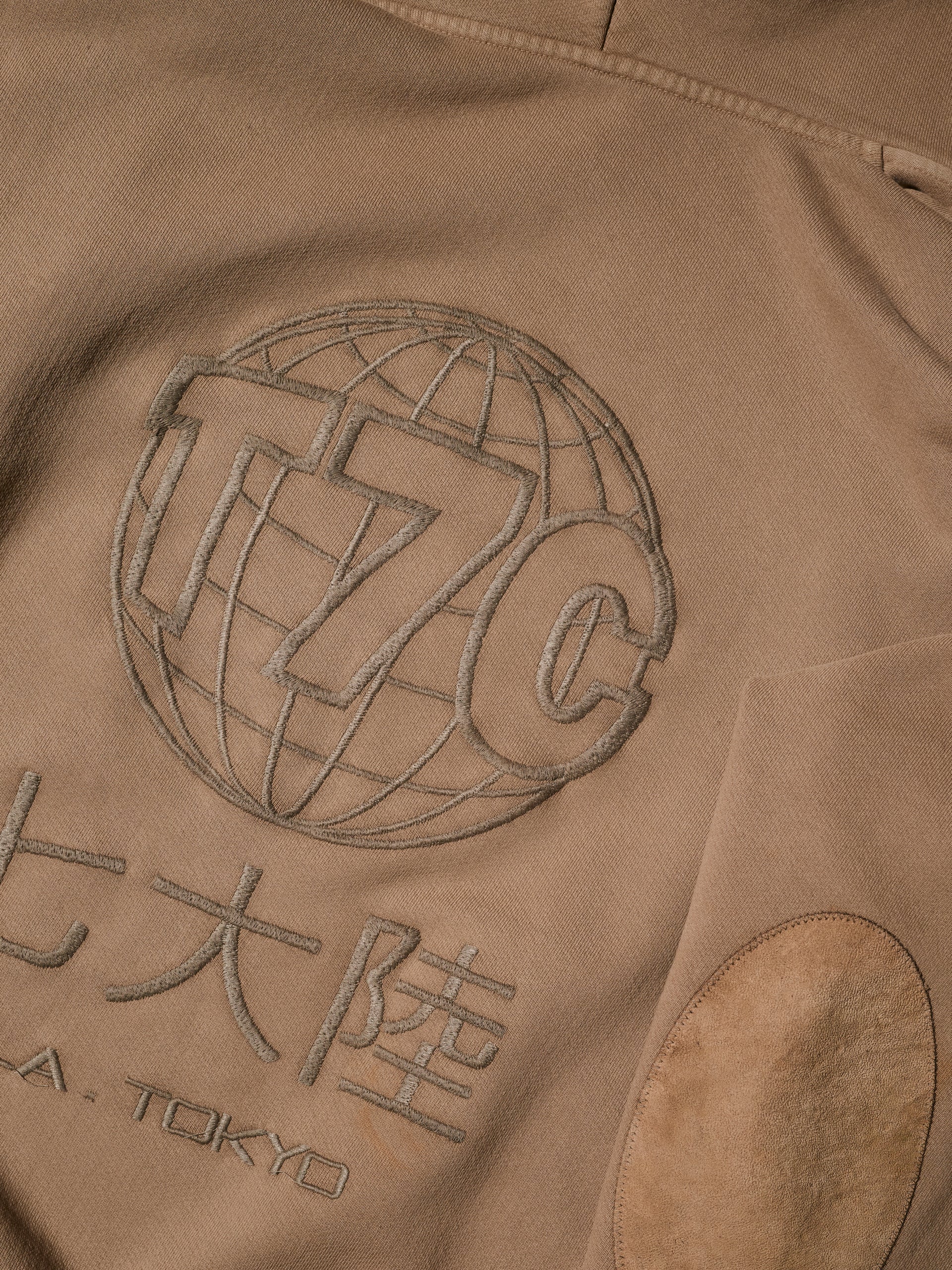 A detail image of a logo on the back of a tan hoodie