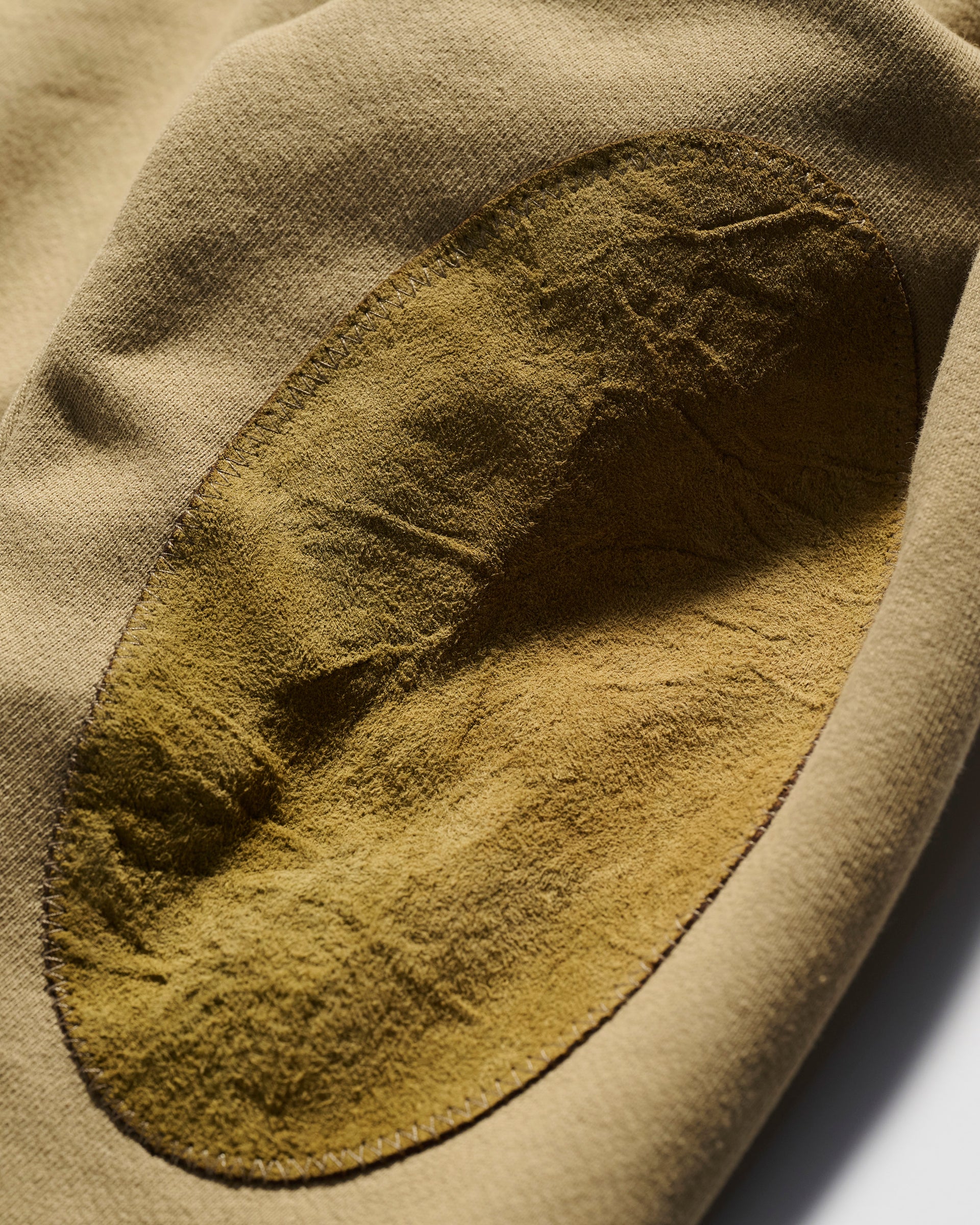 A close-up of the tan Camden Hoodie in Desert by T7C The Seven Continents, showing an oval suede textured elbow patch stitched on the sleeve.