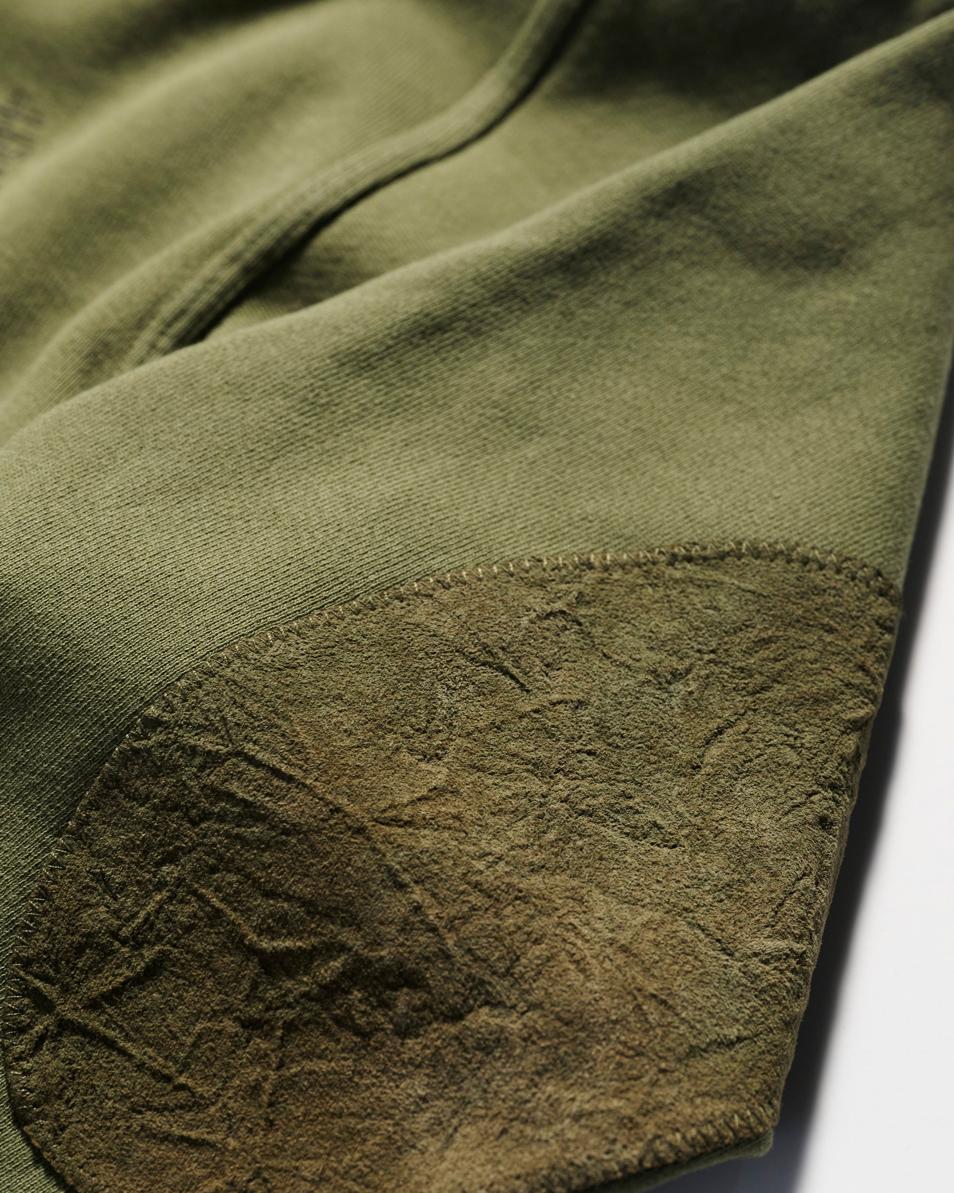 Close-up of olive green fabric with a textured, darker green suede elbow patch—an elevated detail on the relaxed fit Camden Hoodie in Olive by T7C The Seven Continents.