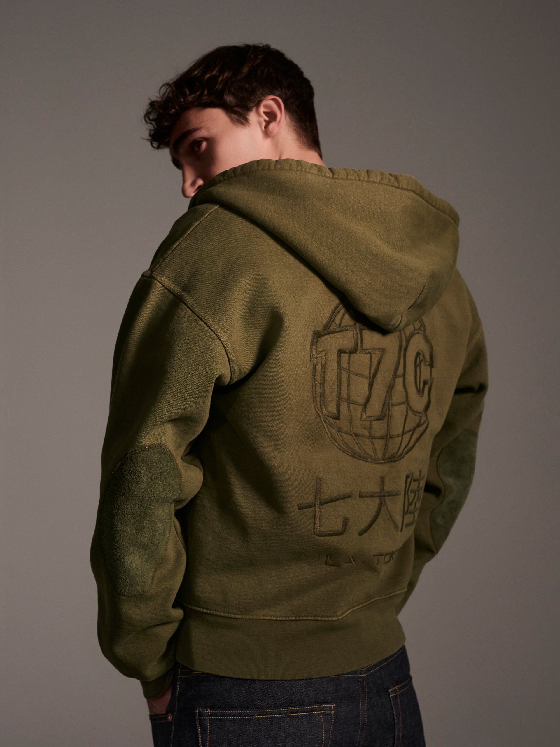 A back image of a male model in an olive zip-up hoodie