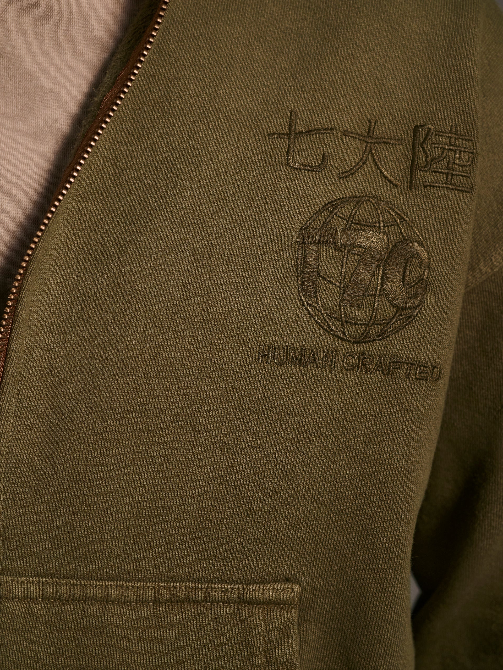 A detail shot of an olive zip-up hoodie with a logo