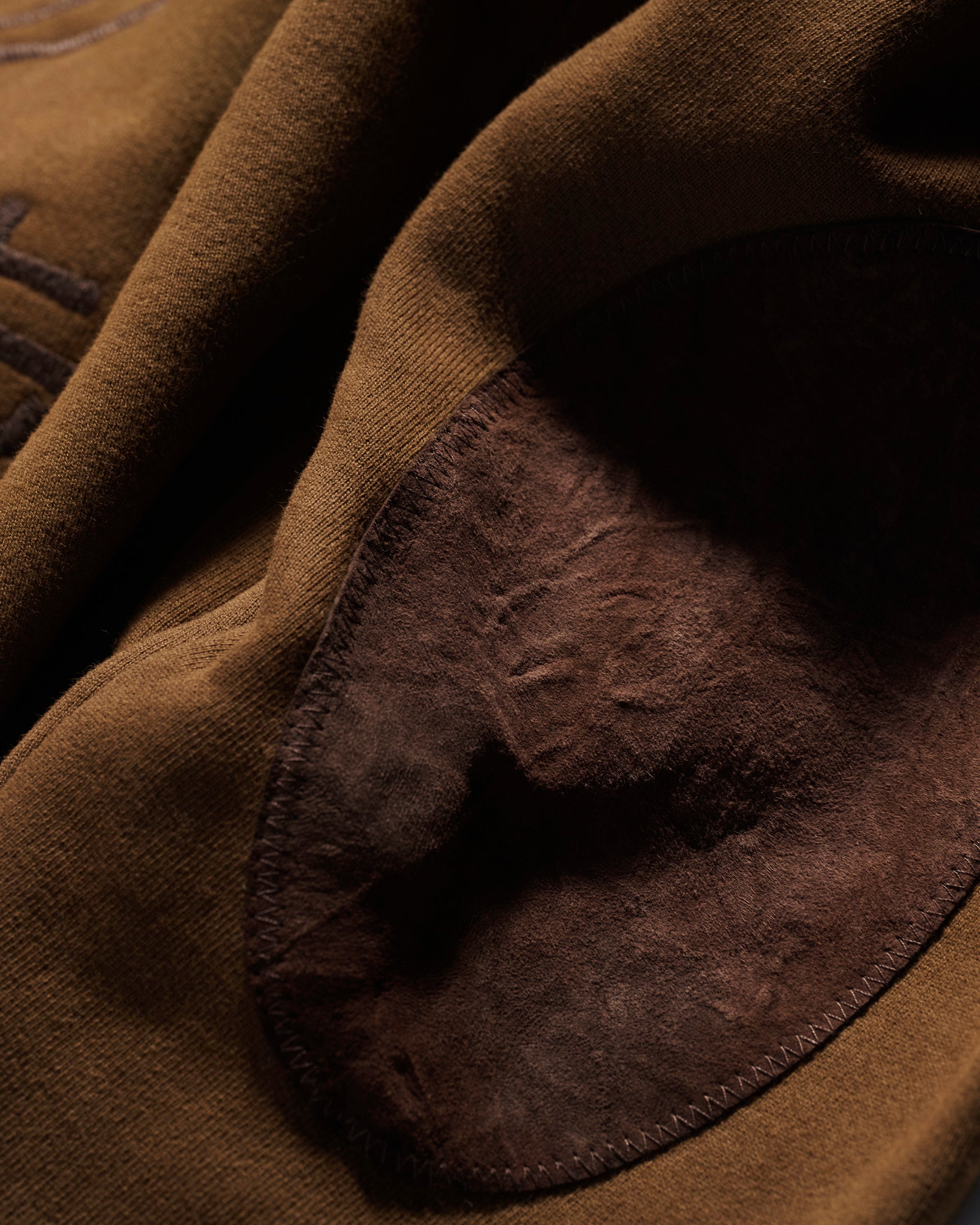 Close-up of the T7C The Seven Continents Camden Hoodie in Pecan shows its brown fabric with a darker suede elbow patch, highlighting the contrast between the smooth material and soft, textured suede.