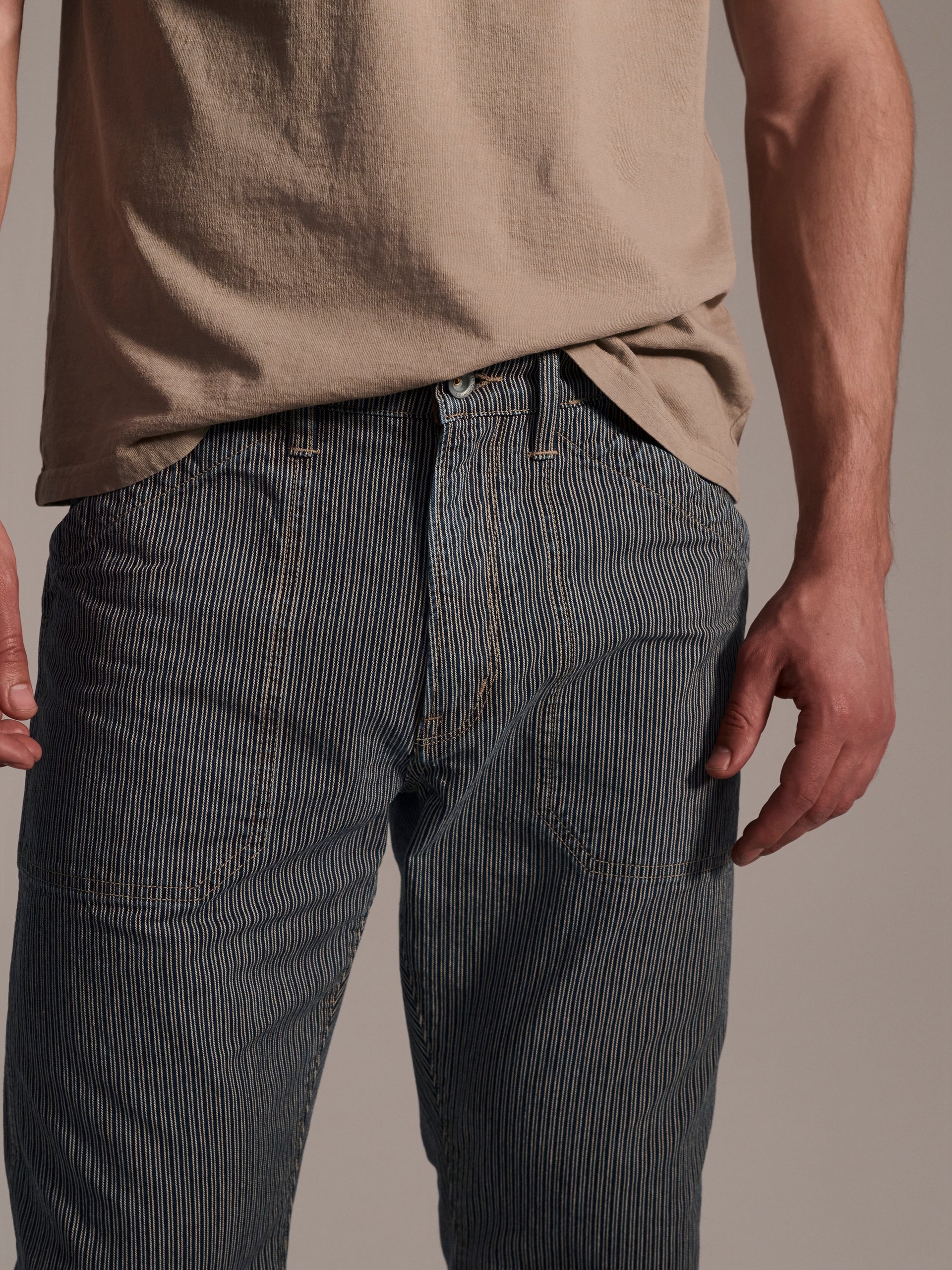 A detail image of a male model wearing blue and white railroad stripe flare pants featuring workwear-style front pockets