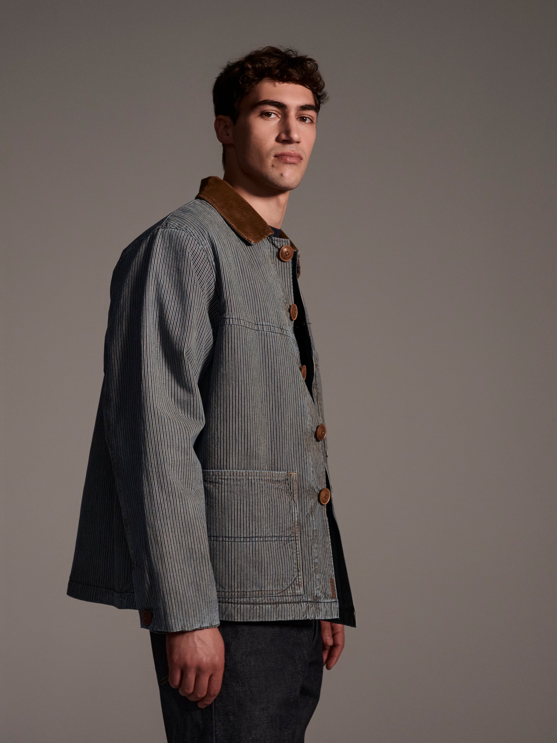 A profile image of a male model wearing a blue and white railroad stripe jacket with a corduroy collar