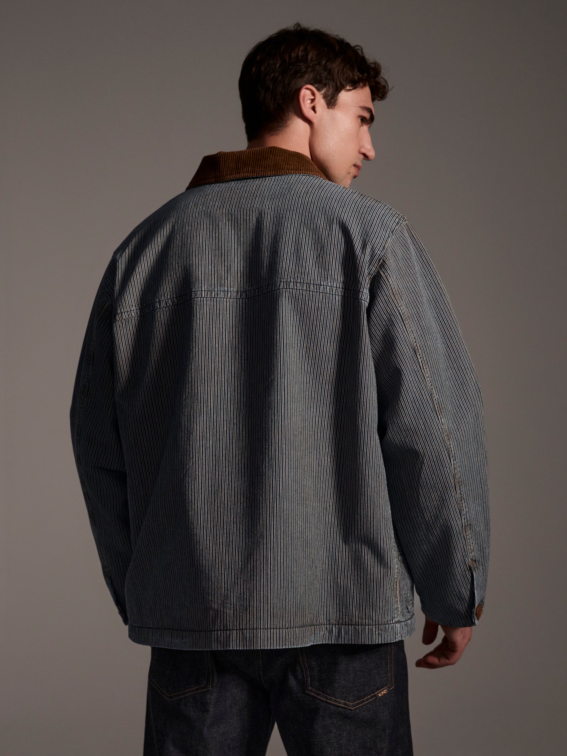 A back image of a male model wearing a blue and white railroad stripe jacket with a corduroy collar