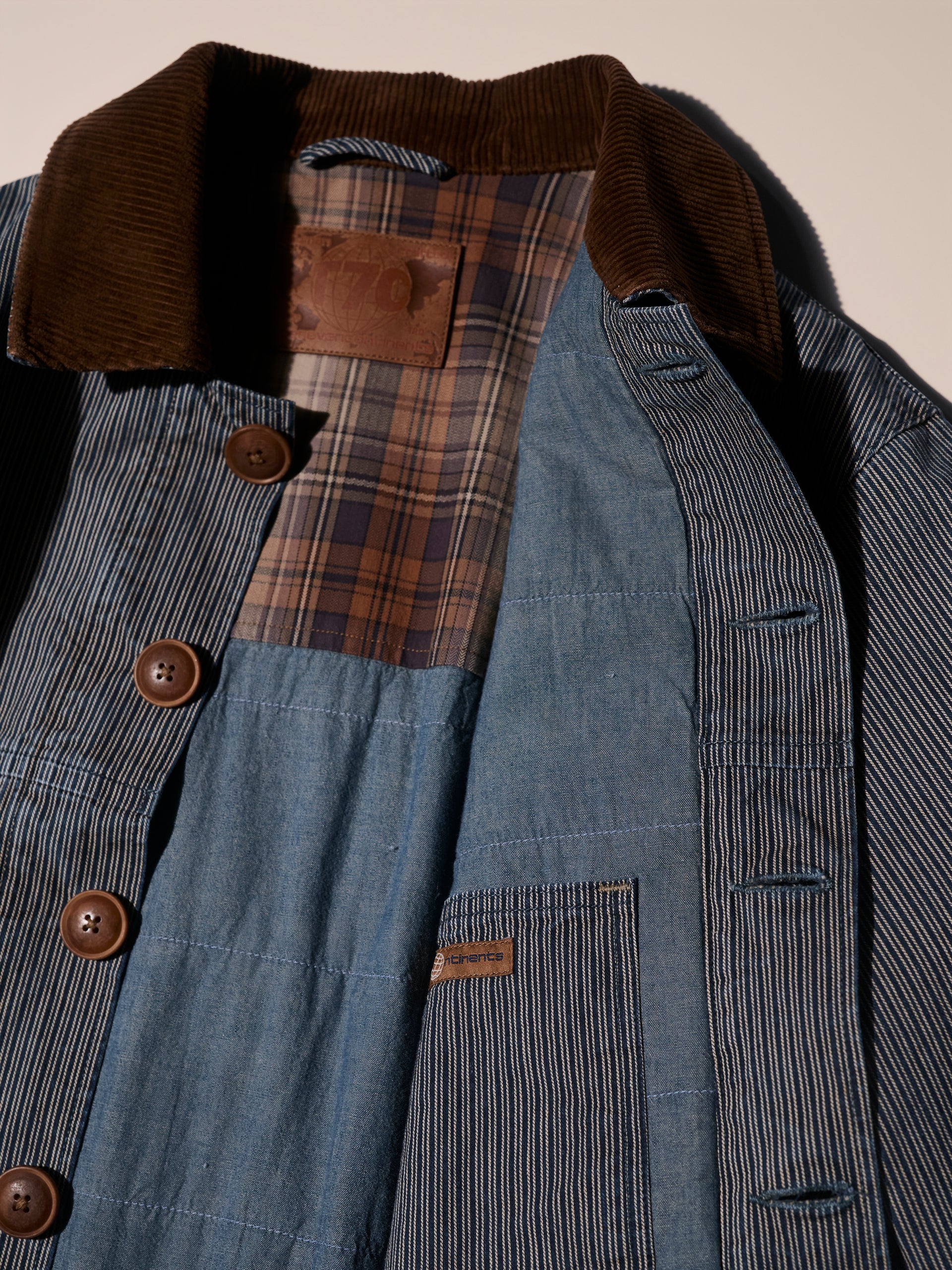 A flat lay image of a blue and white railroad stripe jacket with a corduroy collar