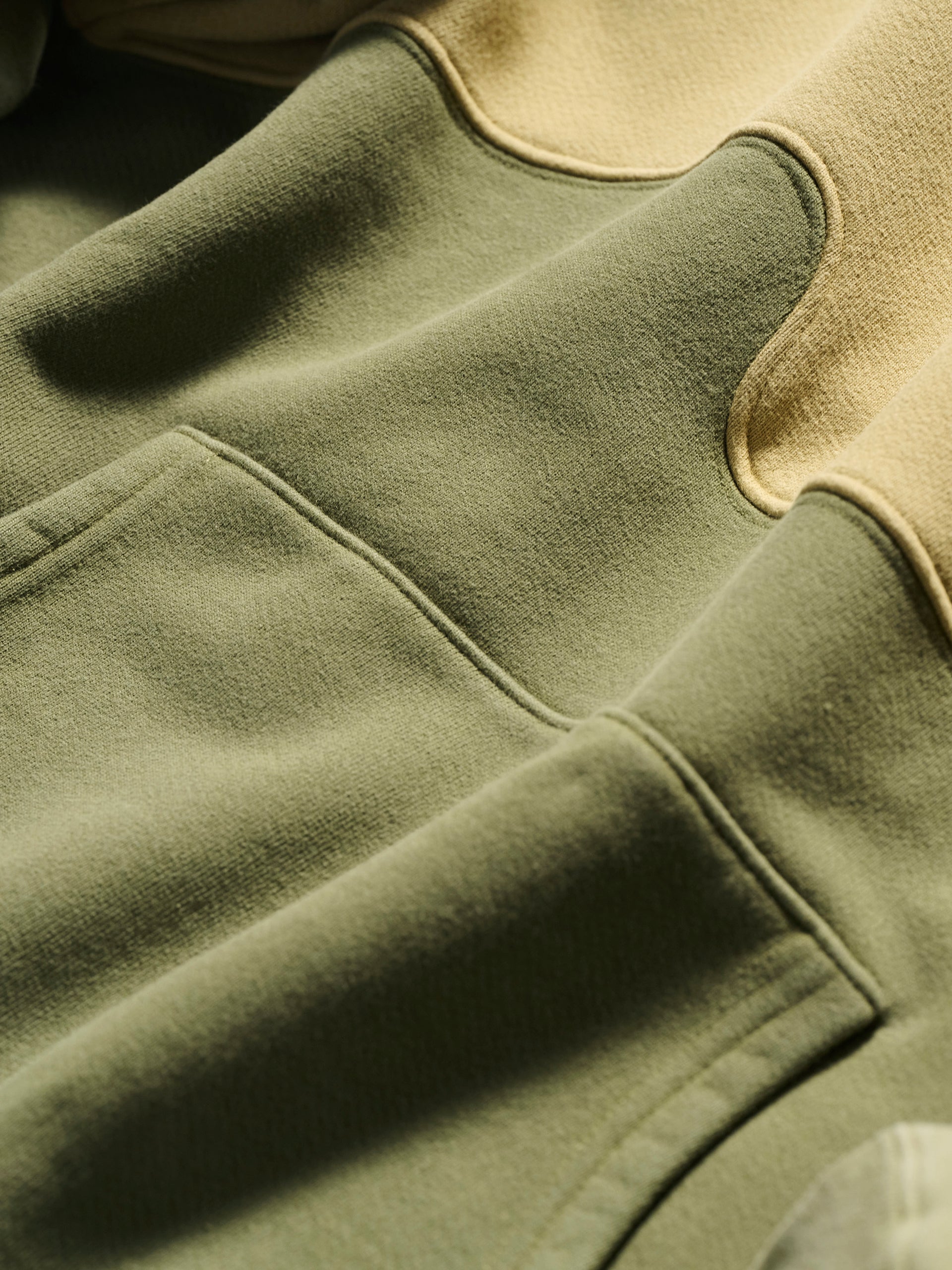 Close-up of The Hunter Hoodie in Verde by T7C The Seven Continents, crafted in soft fabric with neutral olive green and beige tones, camo-inspired seam stitching, and a spacious front pocket.