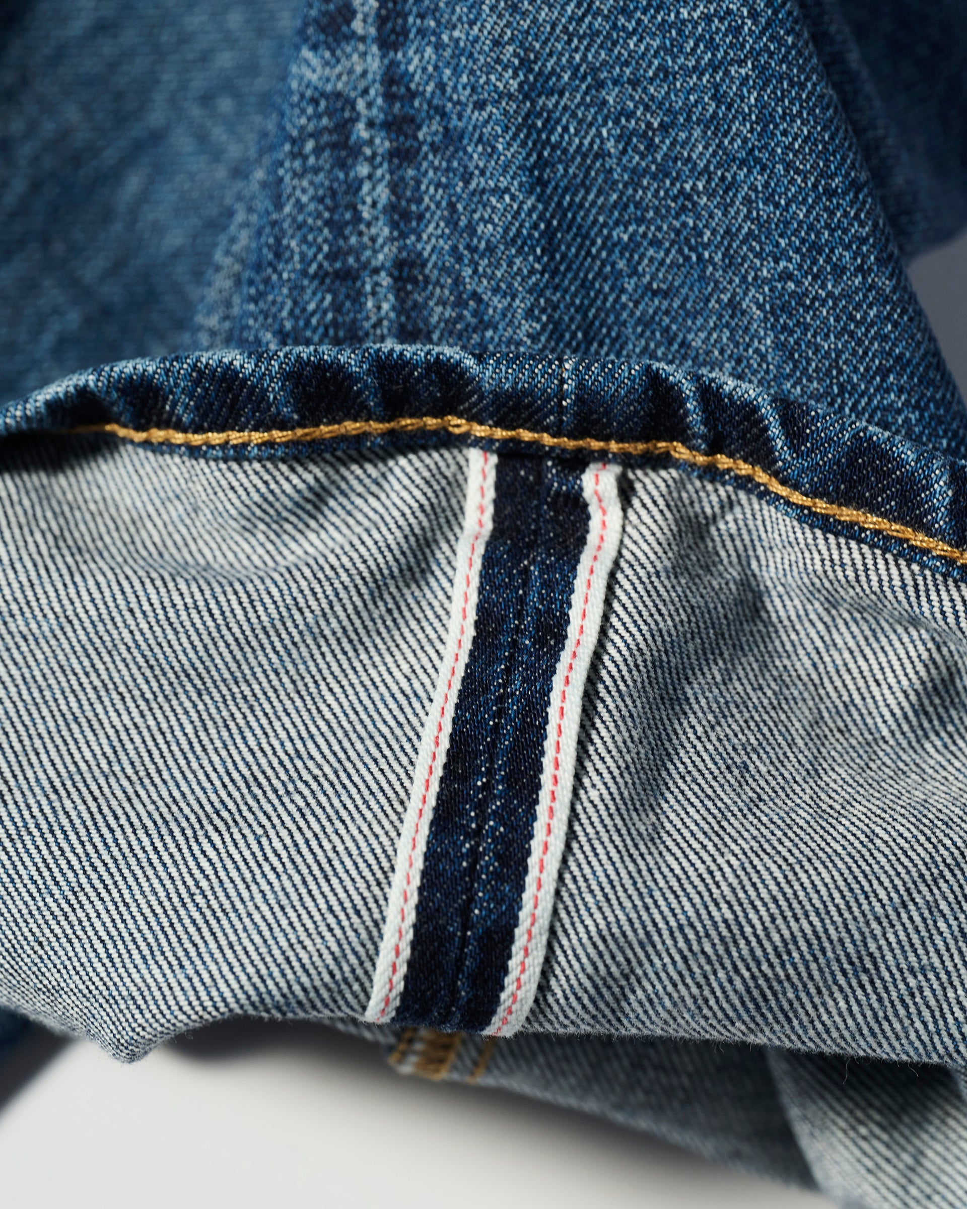 A close-up of the cuff of T7C’s The Jack Jean in Tokyo Medium highlights the vintage texture and signature quality of Japanese denim, featuring a selvedge edge with a visible white strip and red stitching.
