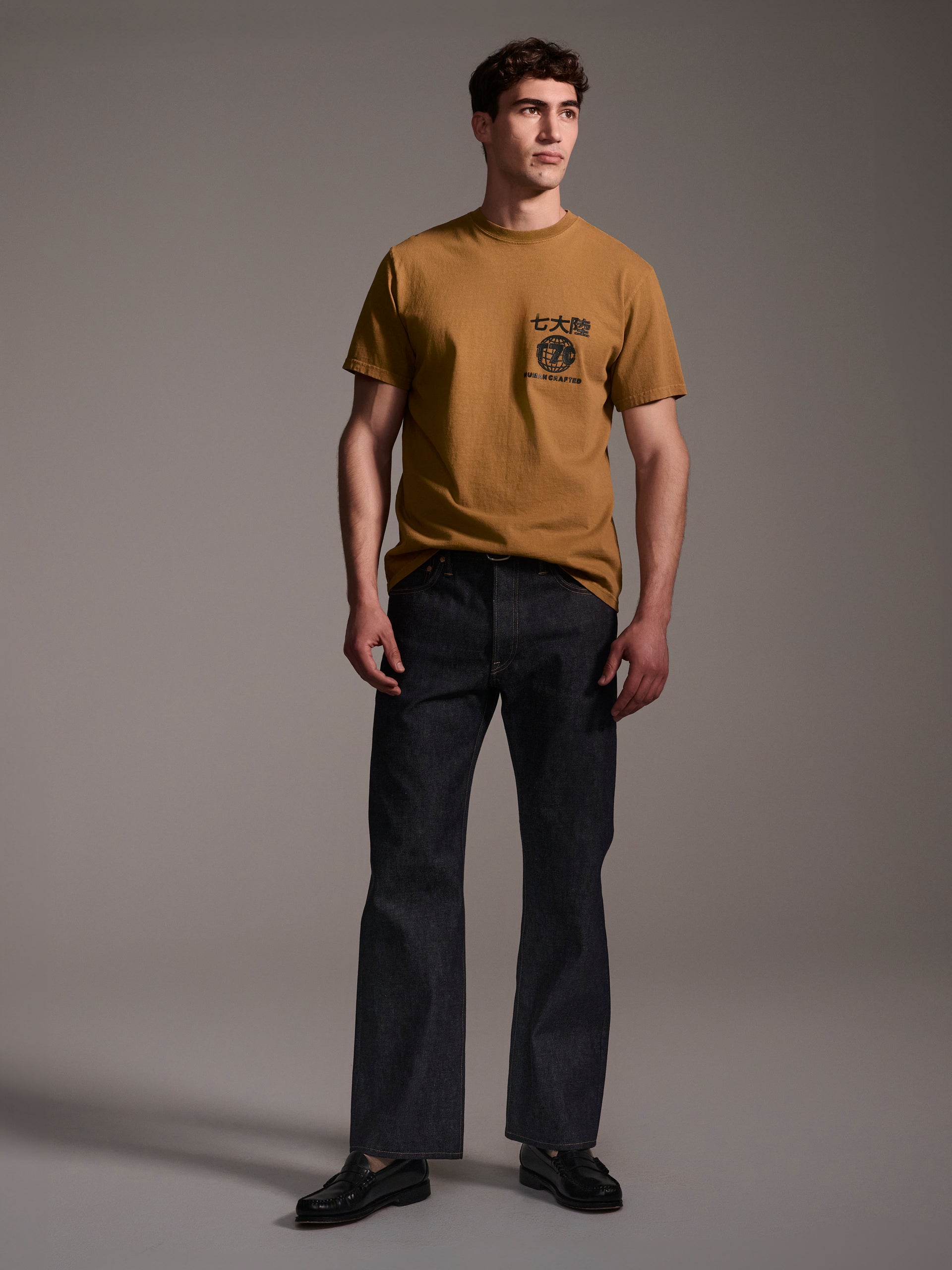 A frontal image of a male model wearing dark blue relaxed fit raw denim jeans