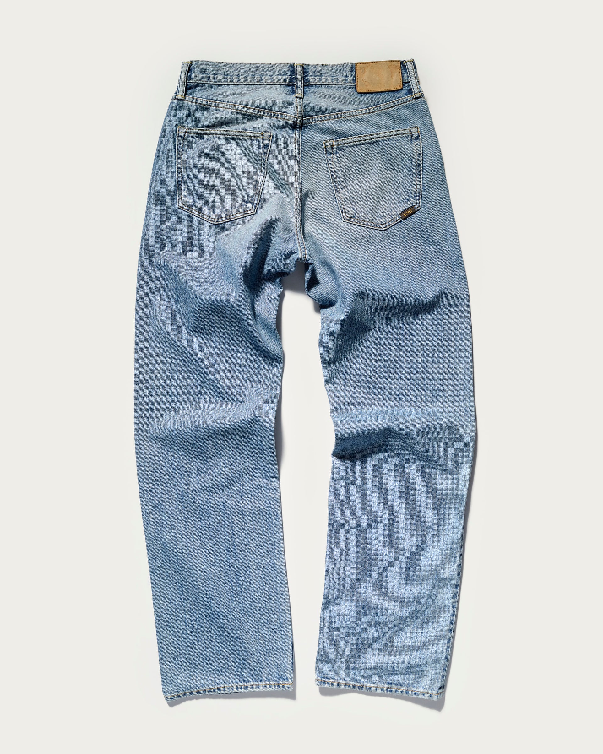 The Jack Jean in Zuma by T7C The Seven Continents is a pair of light blue Japanese denim jeans with two back pockets, a brown leather patch on the waistband, and straight vintage-textured legs, shown flat on a white background.