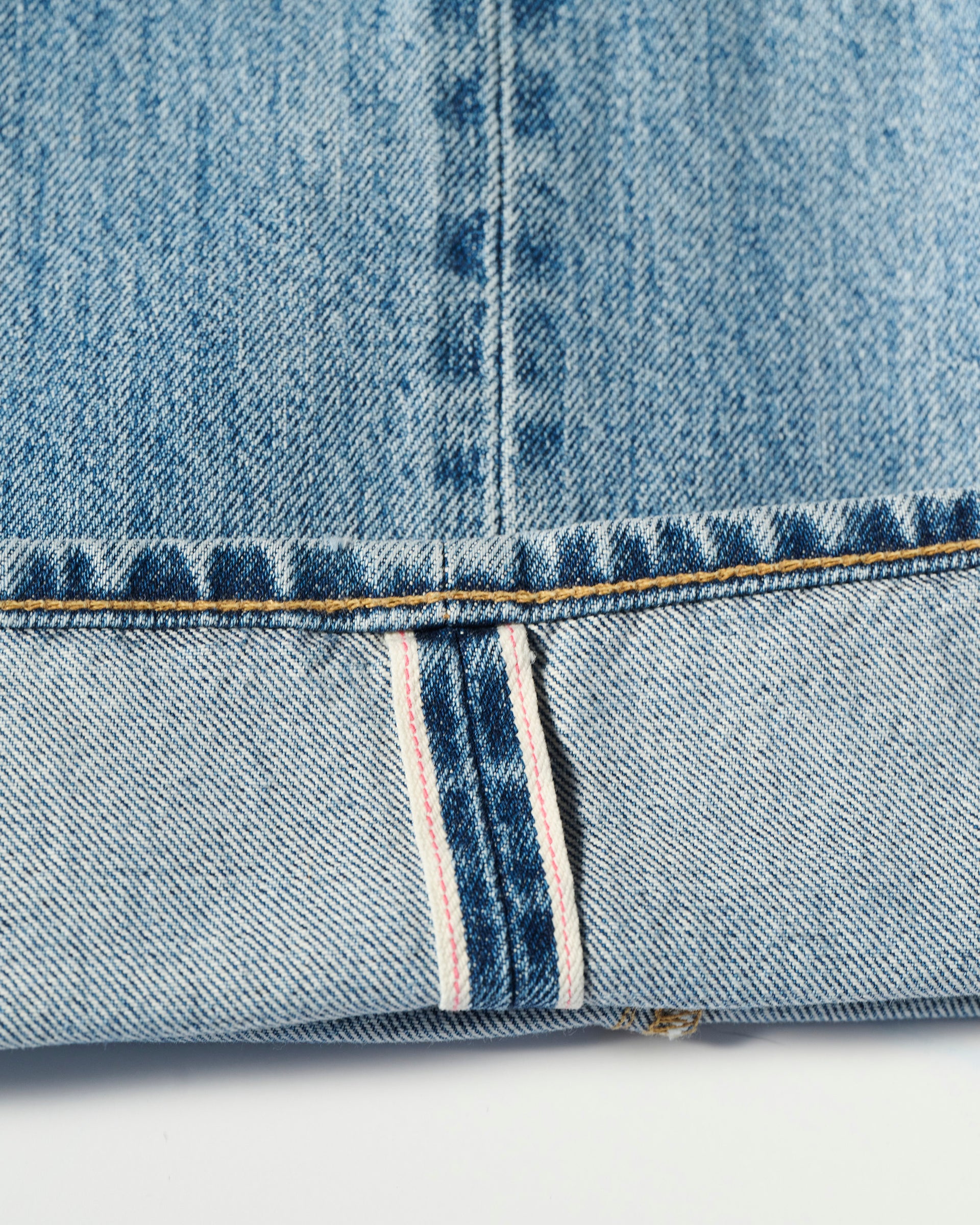 Close-up of The Jack Jean in Zuma by T7C The Seven Continents: light blue Japanese selvedge denim with a folded cuff, visible white strip, red stitching, and vintage texture highlighting the brands fine craftsmanship.