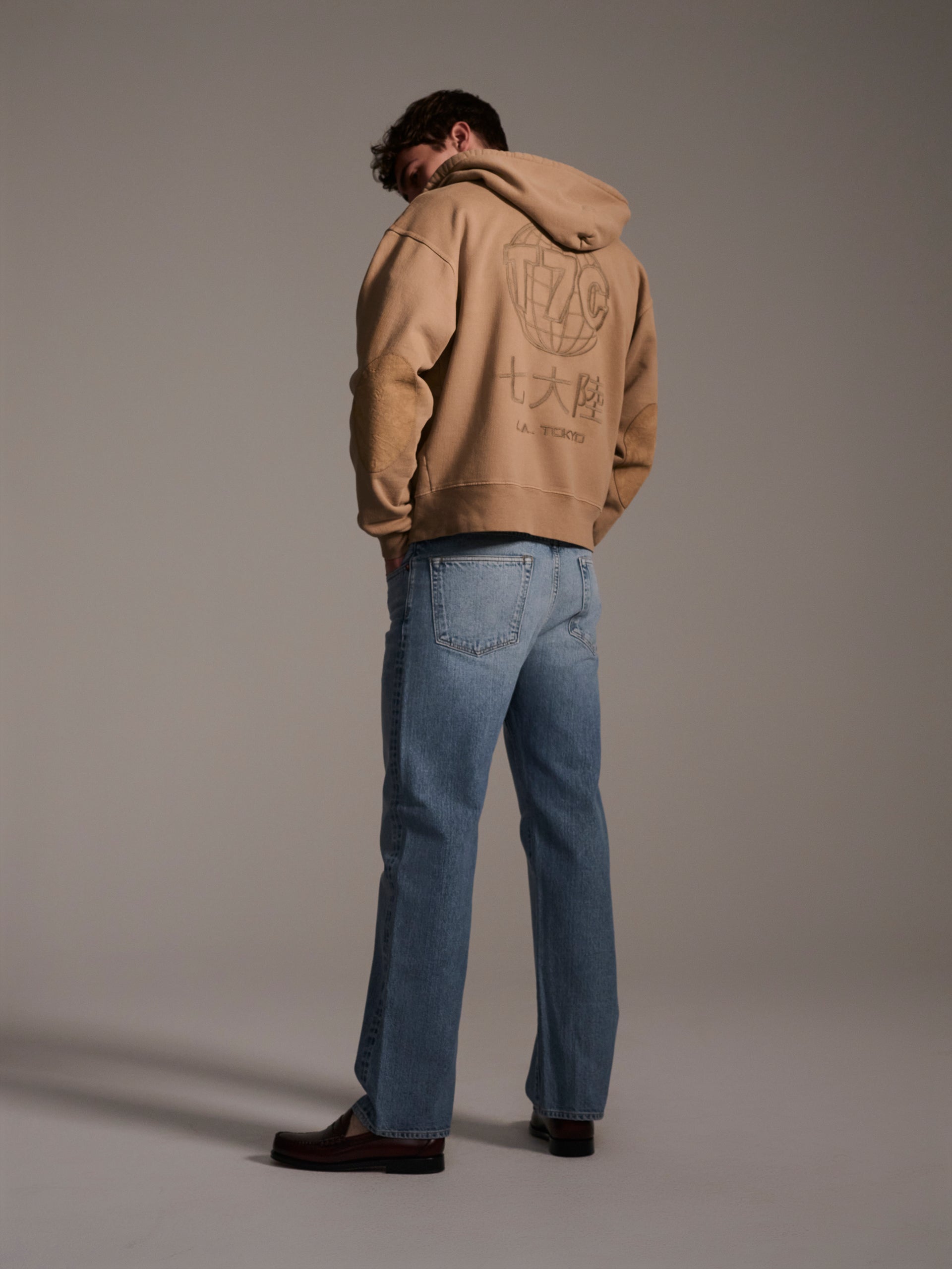 A back image of a male model wearing light blue relaxed fit denim jeans