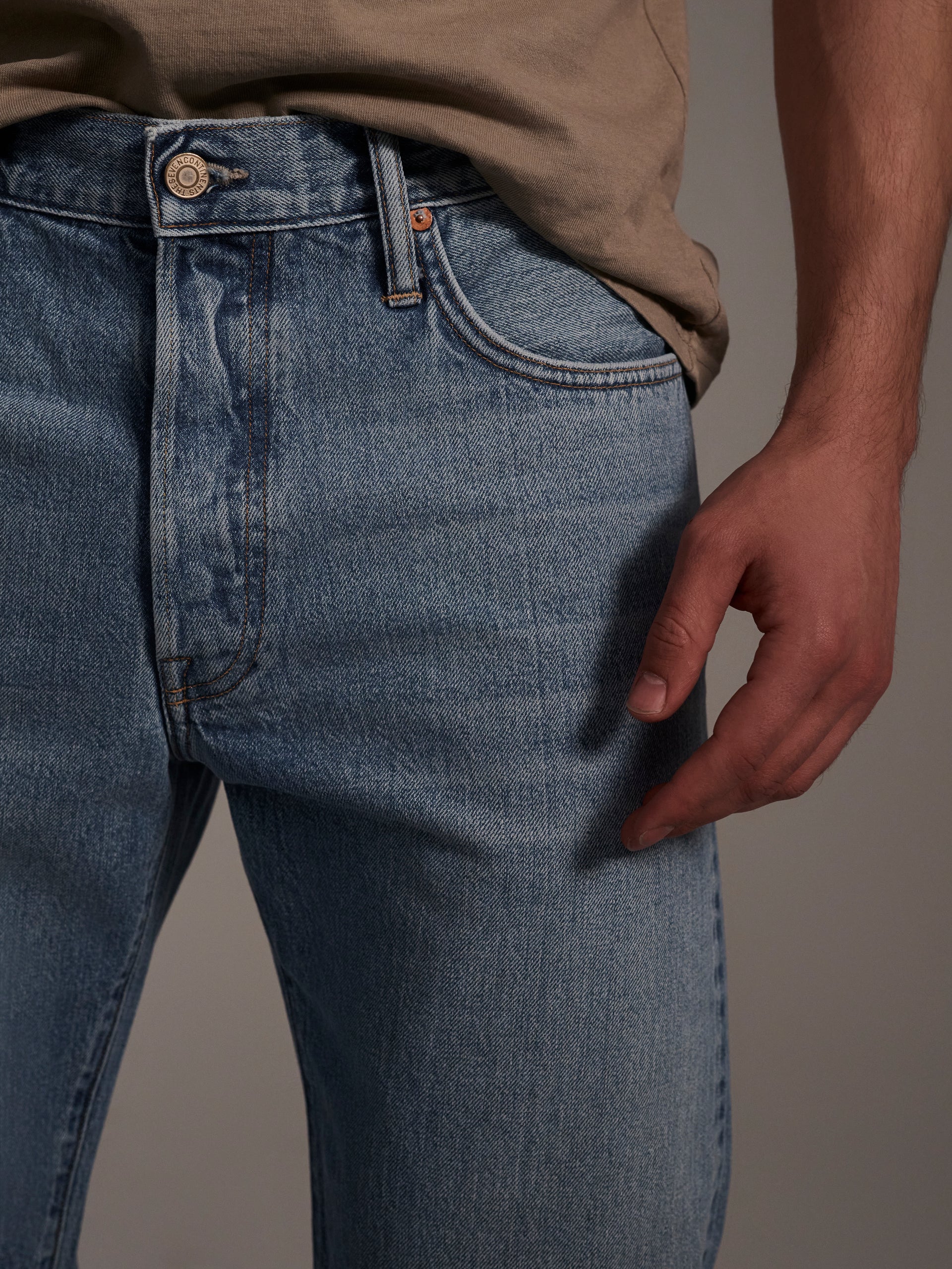 A detail image of a male model wearing light blue relaxed fit denim jeans